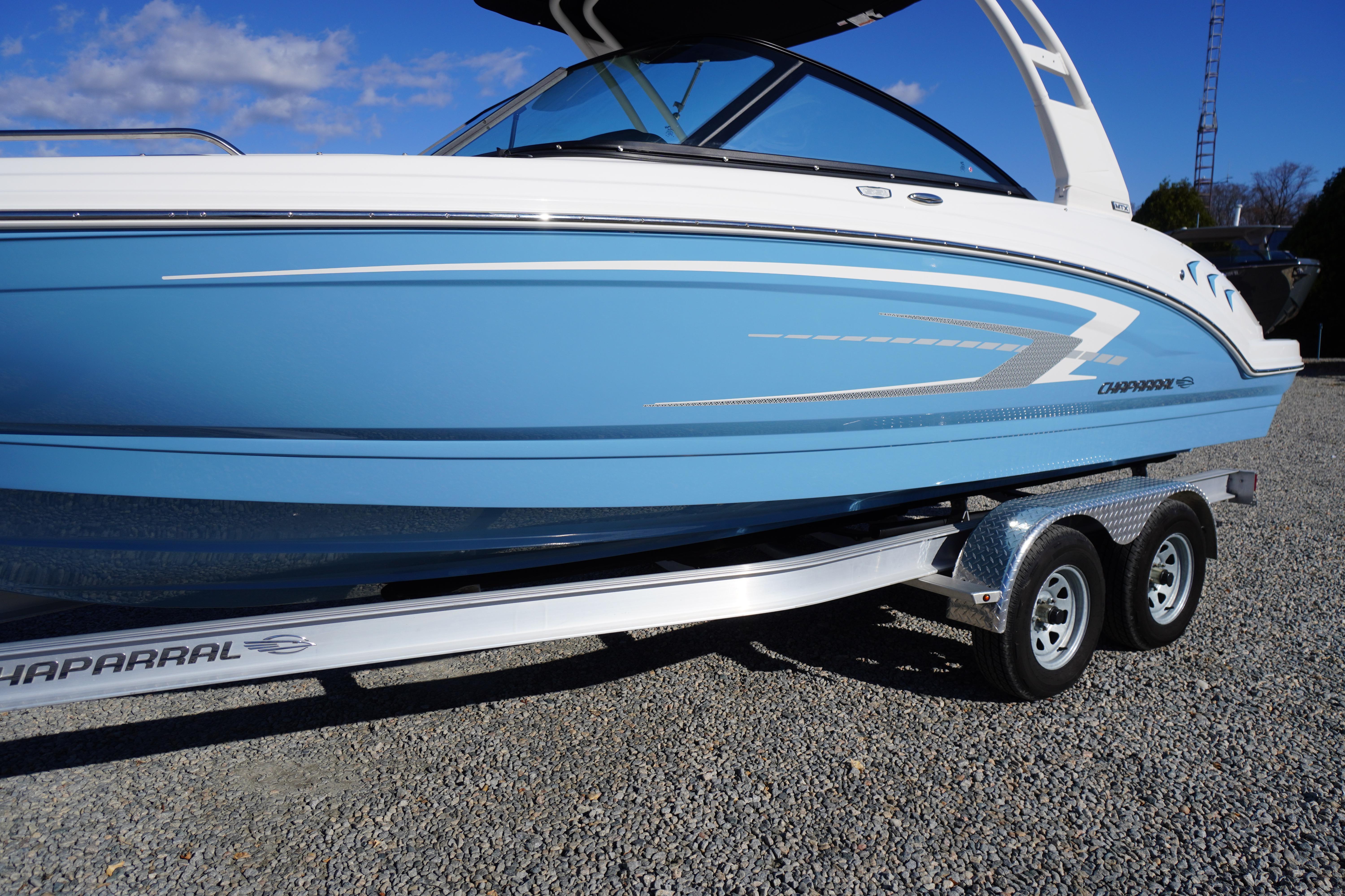 2026 Chaparral 23 SSi boat on trailer, blue and white design, parked on gravel.