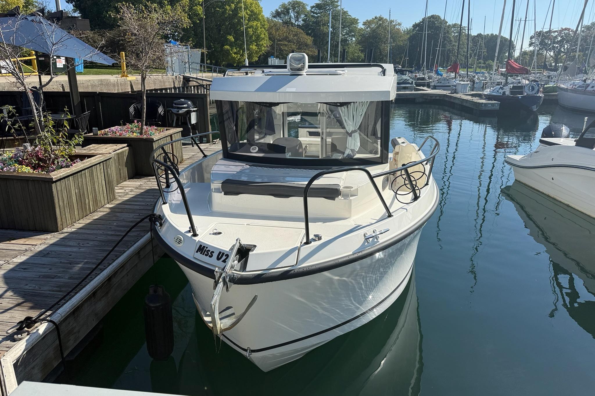 2024 Bayliner Trophy T25 Pilothouse docked at marina, surrounded by boats and greenery.