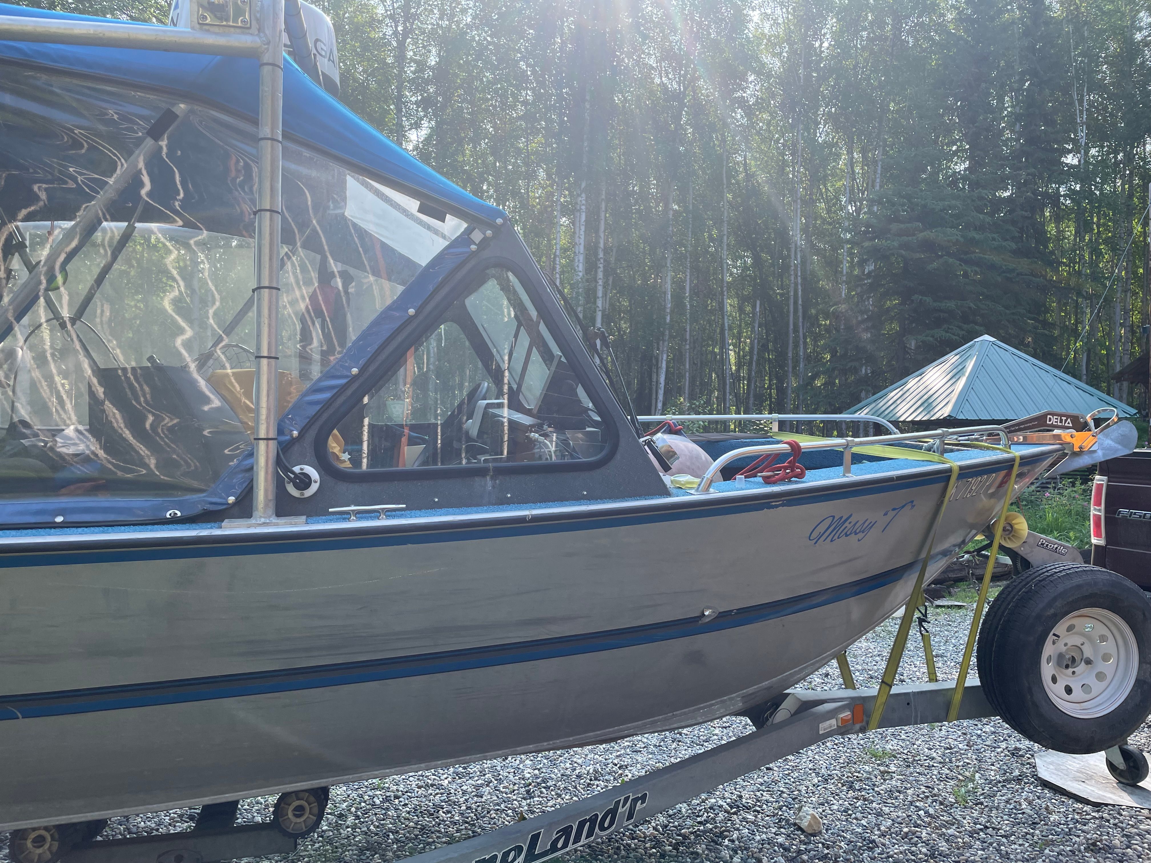 A 1998 Hewescraft Sea Runner 210 boat on a trailer in a wooded area.