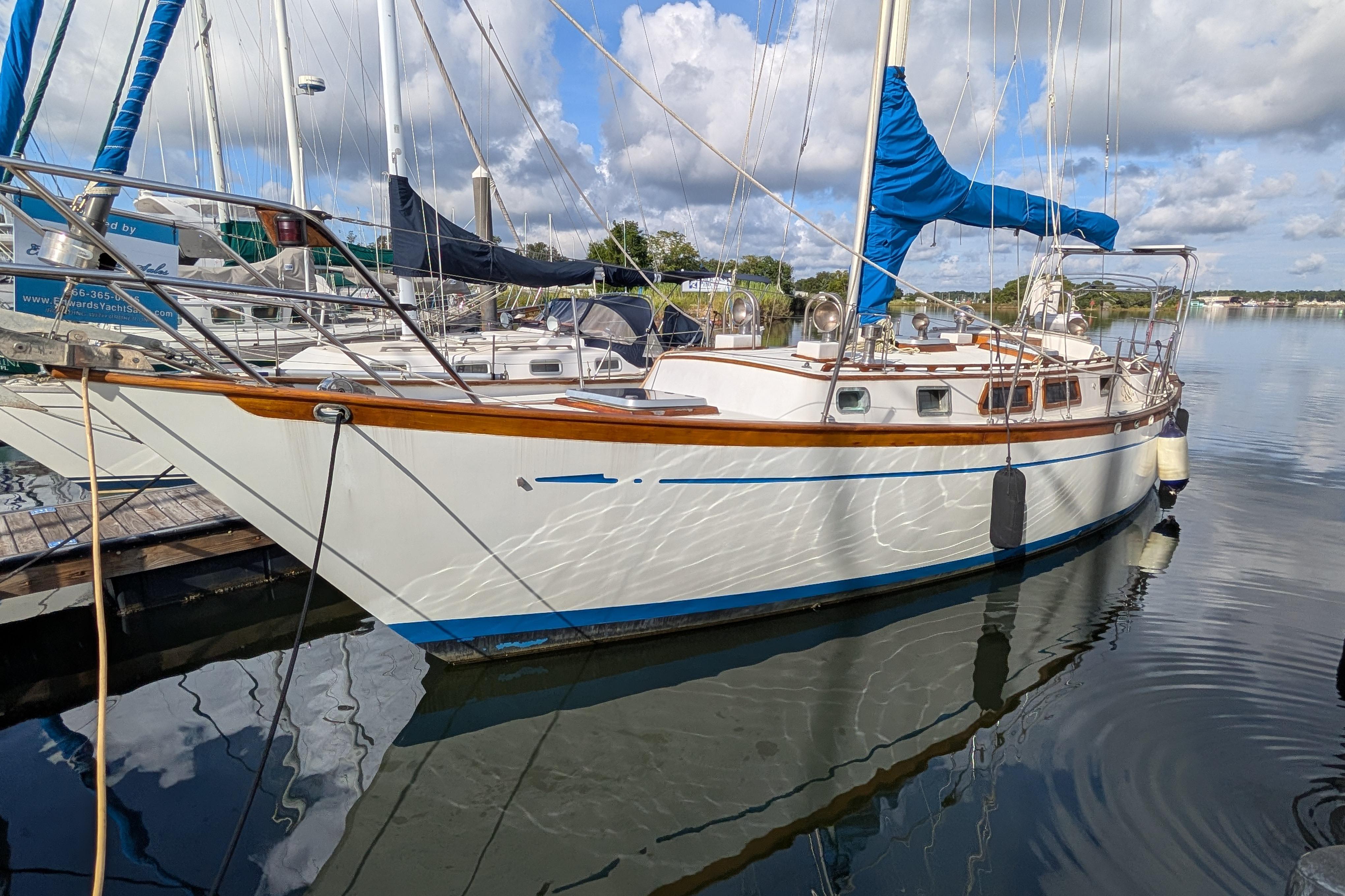 1983 Robert Perry 41 sailboat docked, reflecting on calm water under a partly cloudy sky.