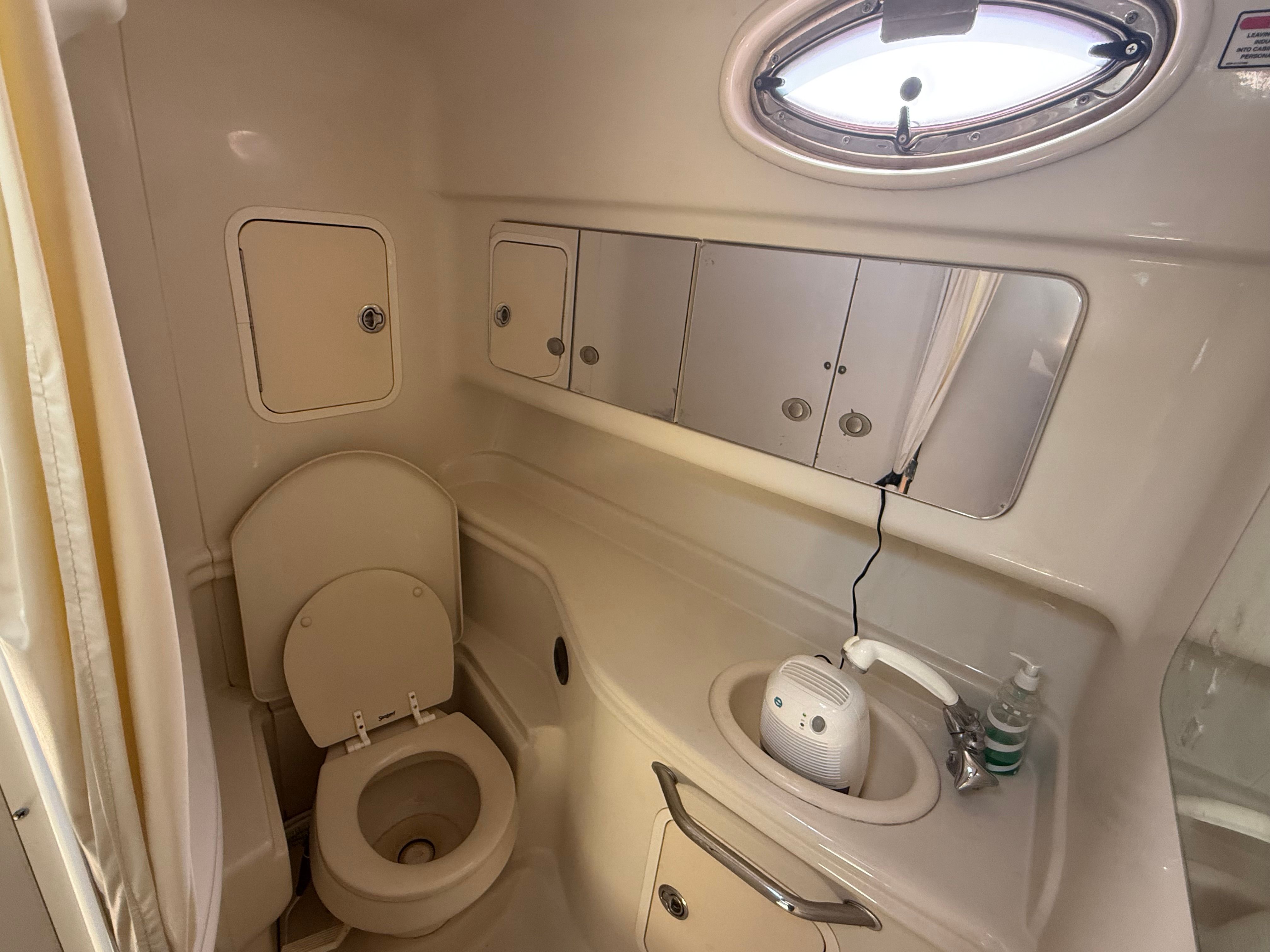 Interior view of a boat bathroom with toilet, sink, and mirrors.