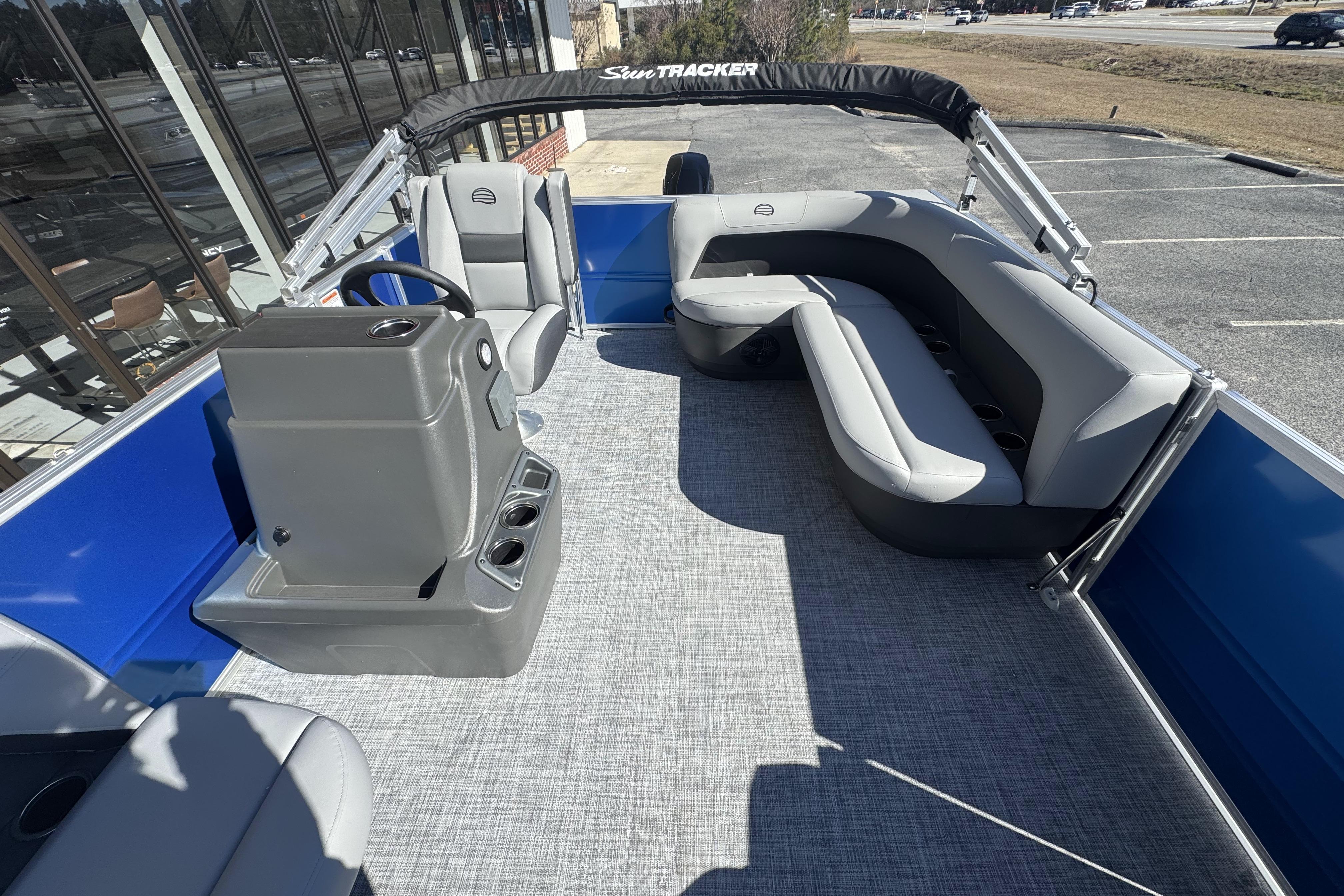 2026 Sun Tracker Party Barge 16 DLX interior with seating and helm, parked outdoors.