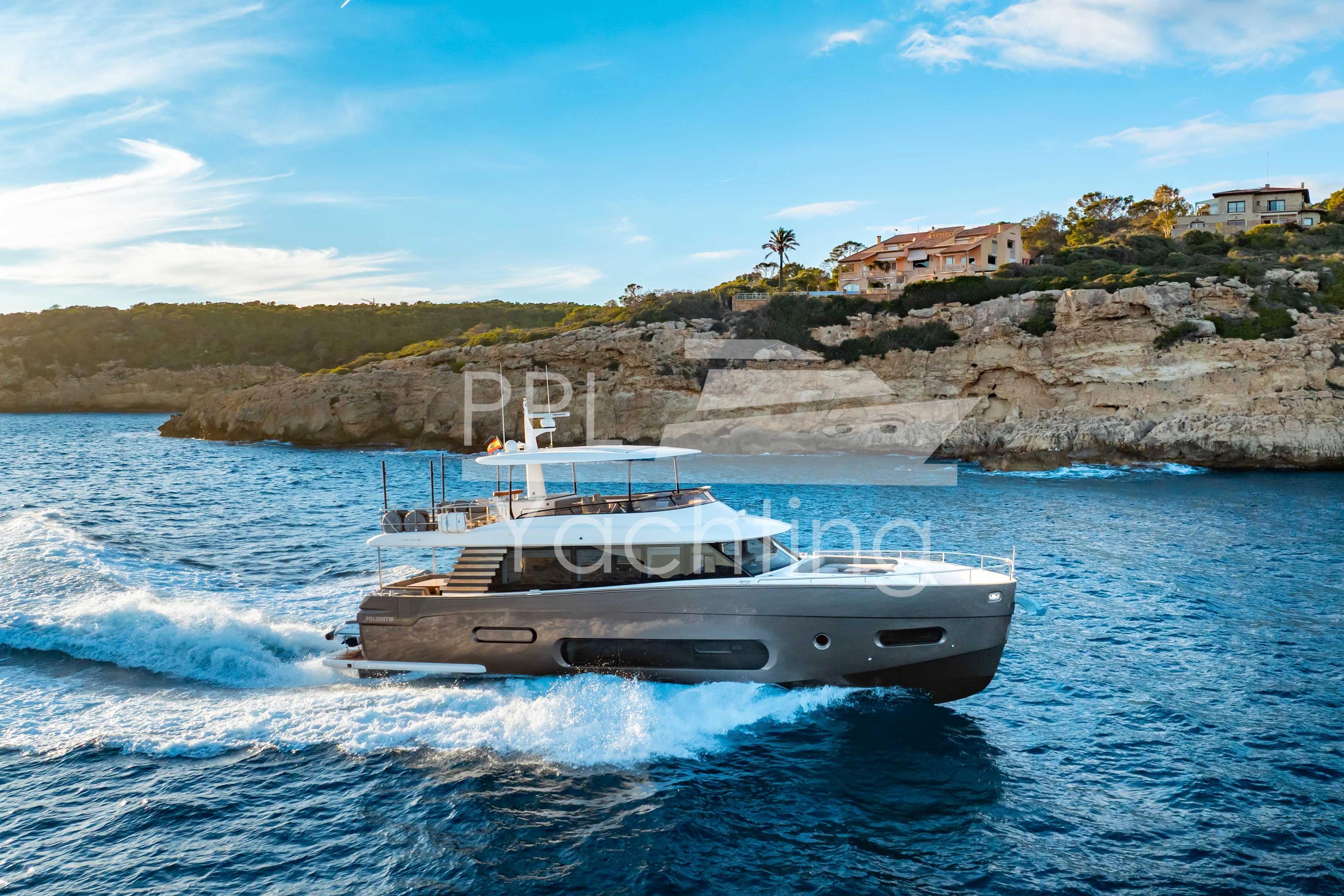 2021 Azimut Magellano 66 yacht cruising near rocky coastline under blue sky.
