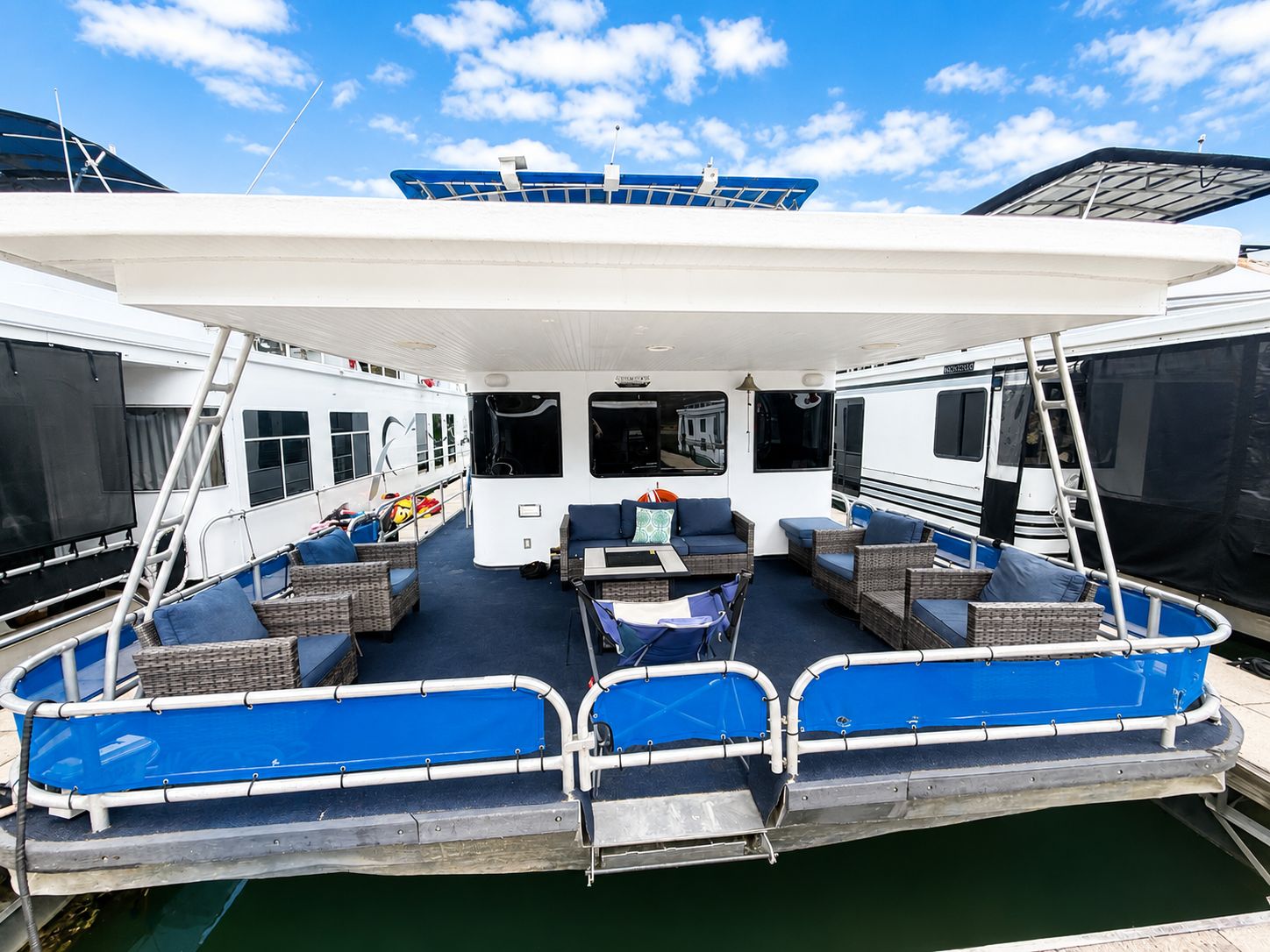 A spacious houseboat with blue accents is docked in the water, surrounded by other boats.