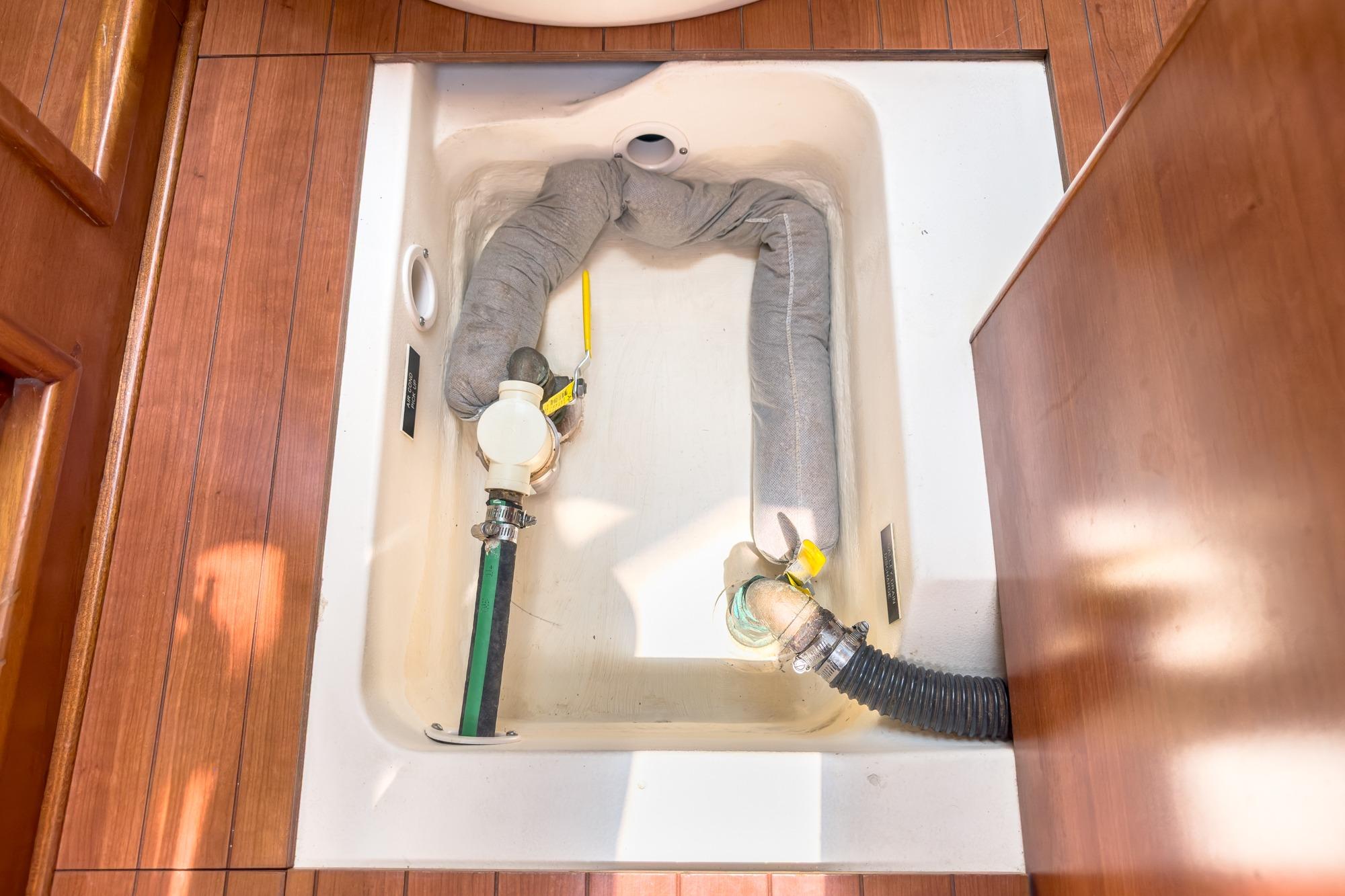 Bilge compartment of 2015 Hunter 33 sailboat with hoses and valves, wooden flooring.