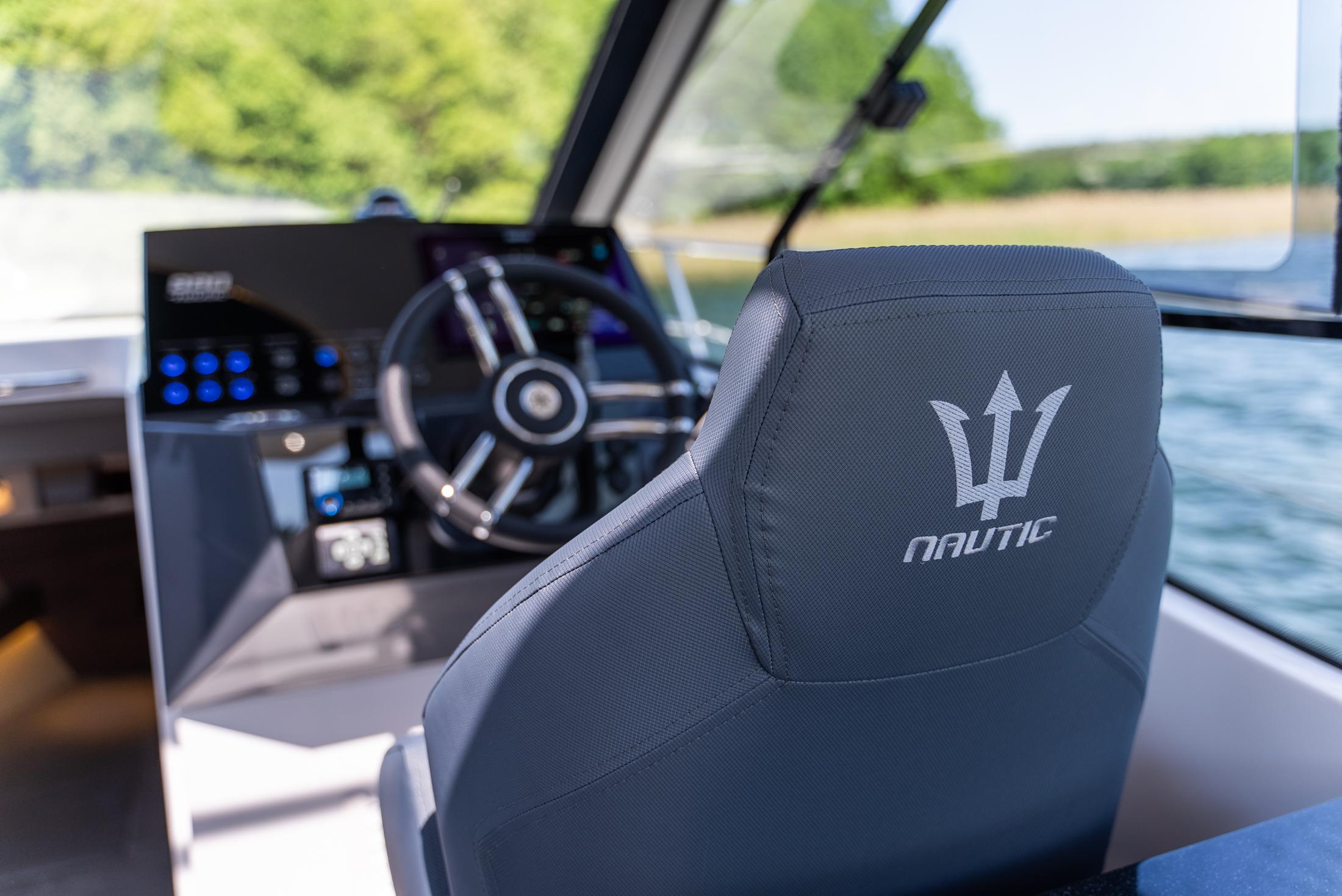 Interior of 2025 Nautic 880 boat, featuring steering wheel and branded seat.