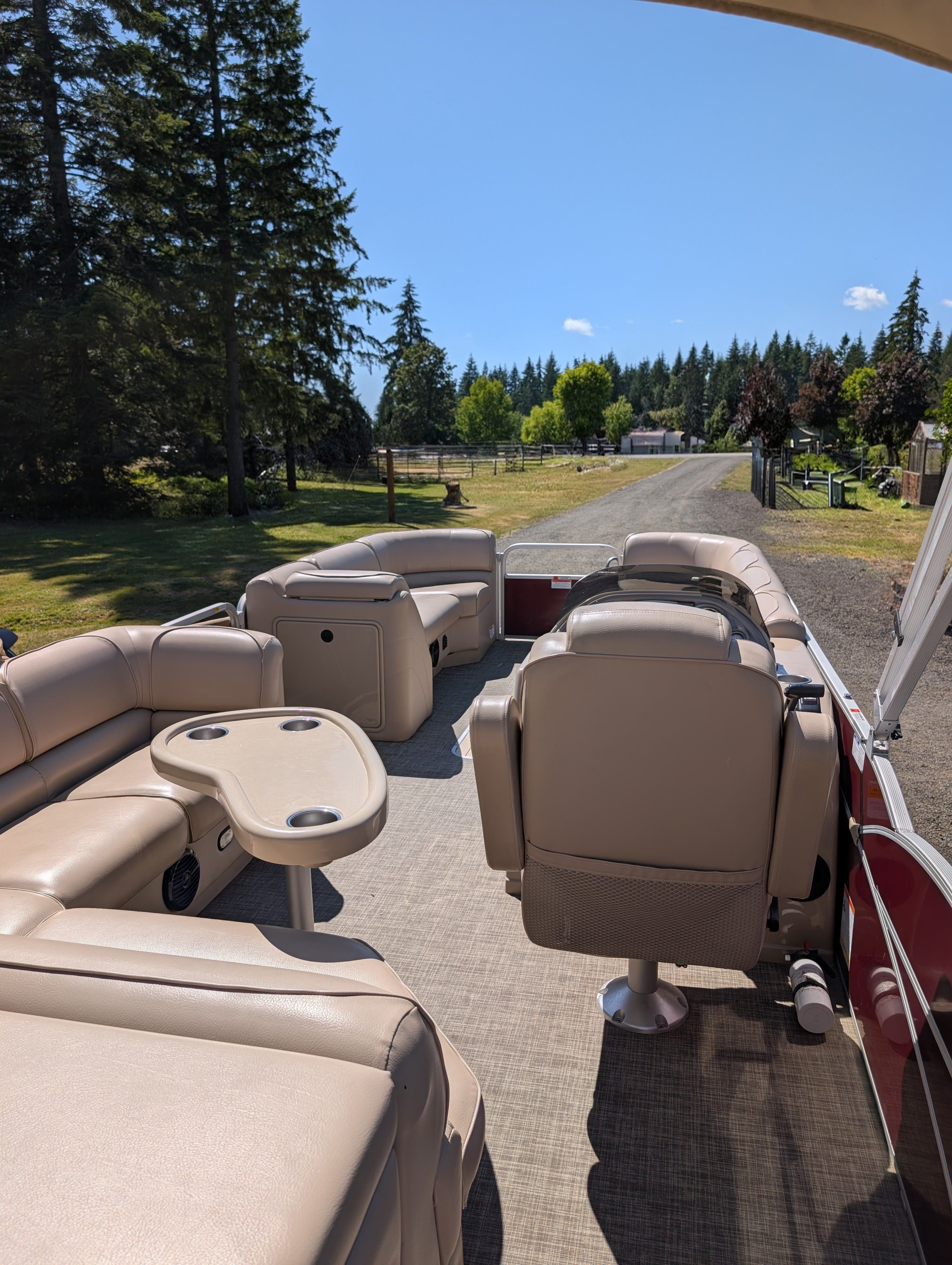Interior of a SunCatcher V322 GX pontoon boat with beige seating and table, surrounded by trees.