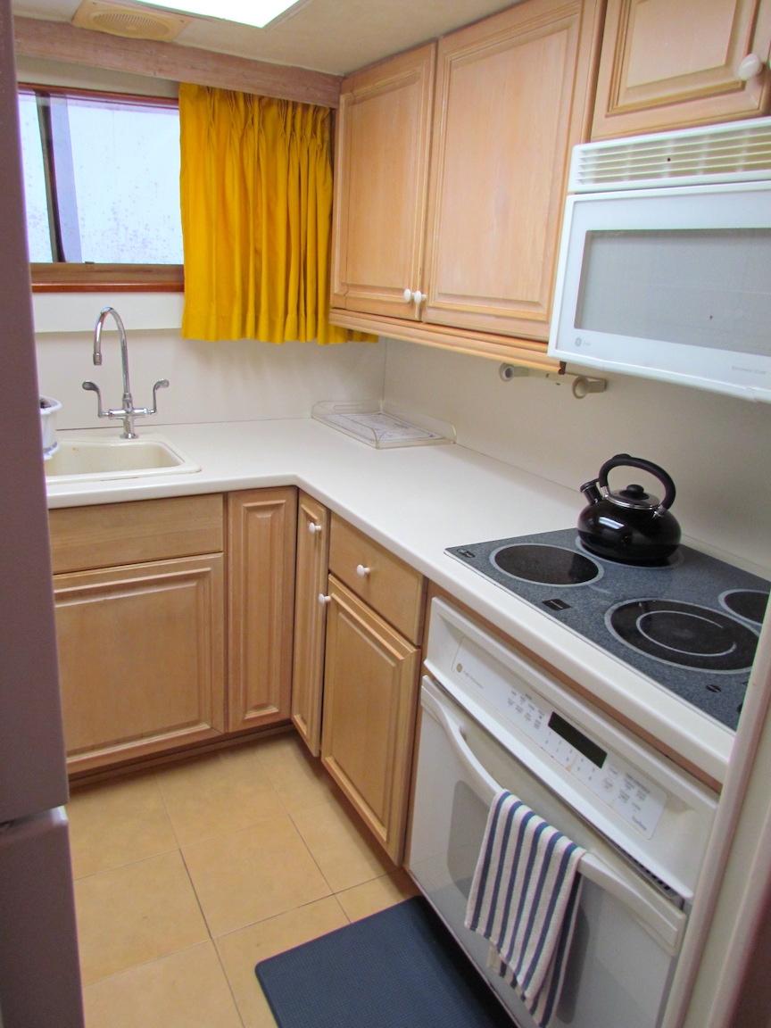 1972 Hargrave 67 Motor Yacht kitchen with wooden cabinets, stove, and yellow curtains.