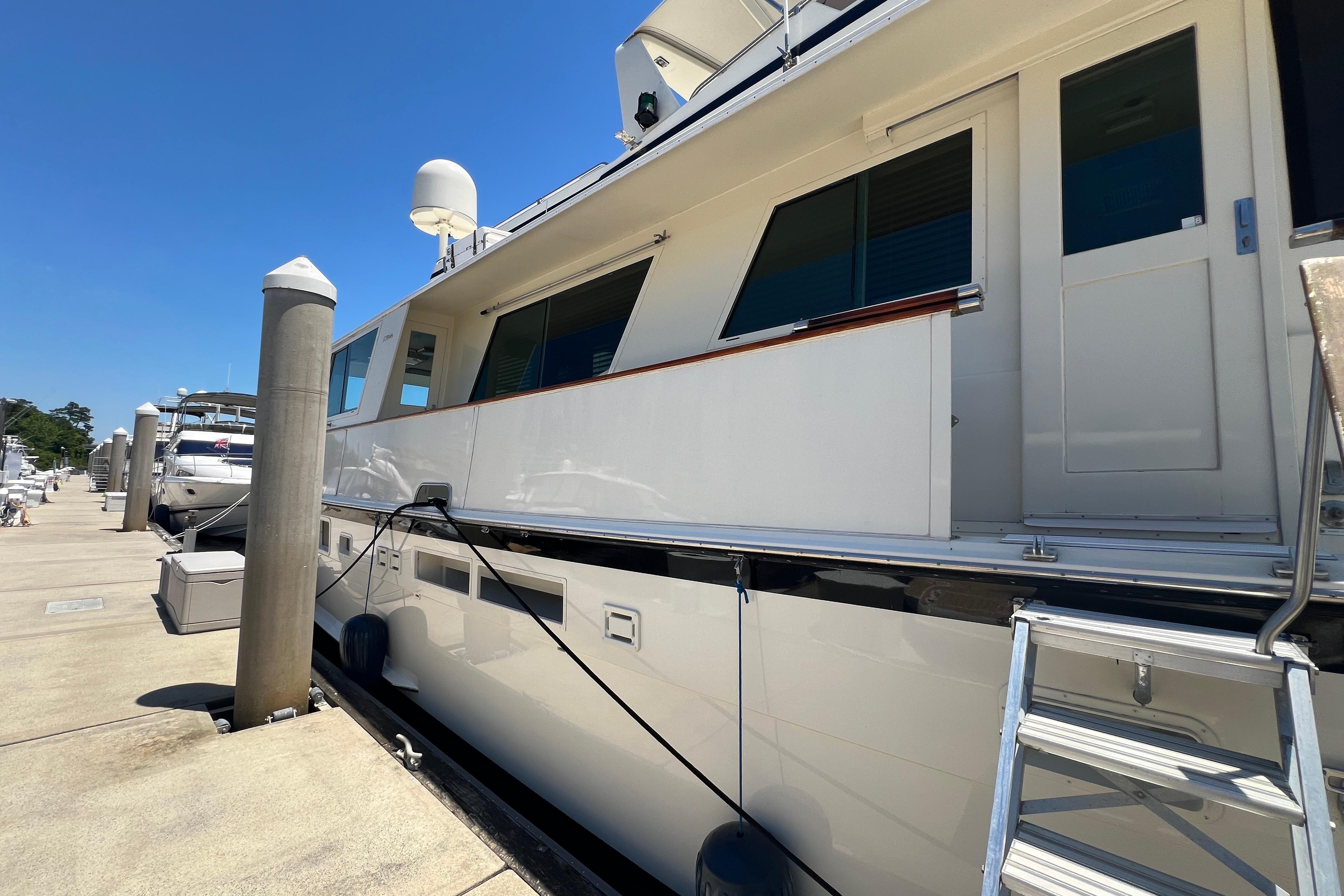 1987 Hatteras 70 Cockpit Motor Yacht docked at marina under clear blue sky.