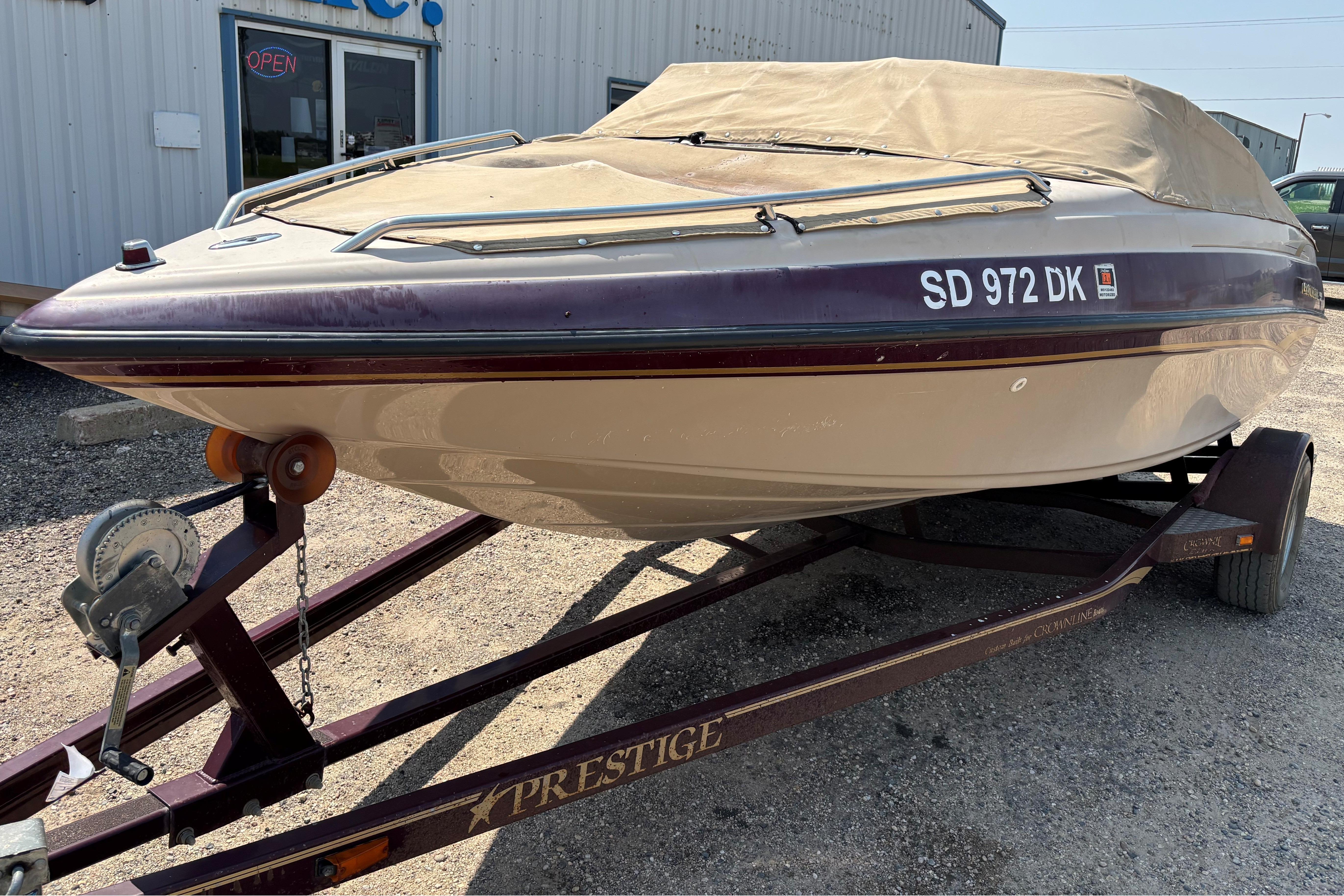 2001 Crownline 18' boat on trailer, covered, parked outside a building.