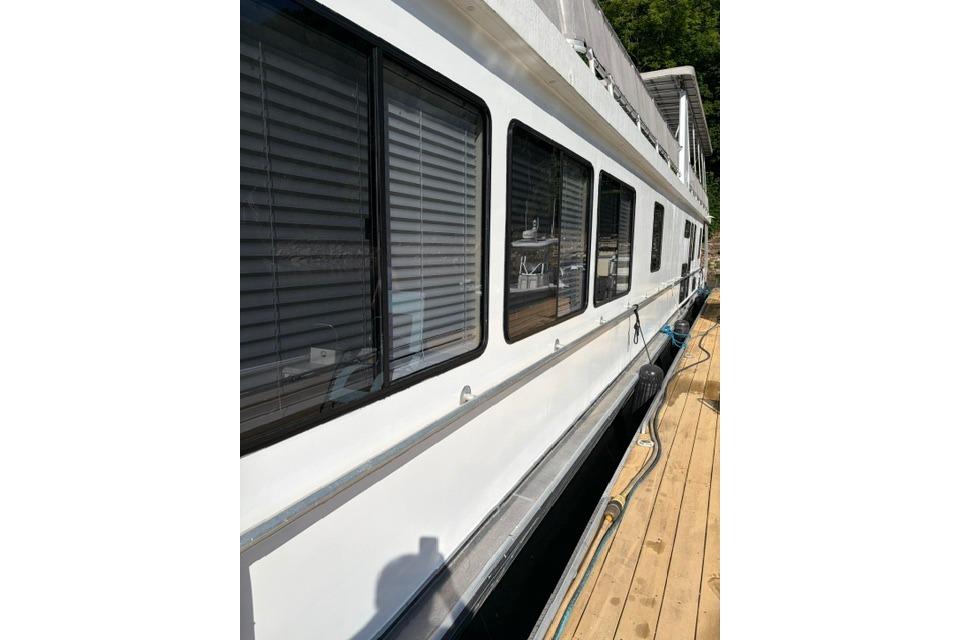 1997 Stardust Houseboat 18x83 docked, featuring large windows and sleek white exterior.