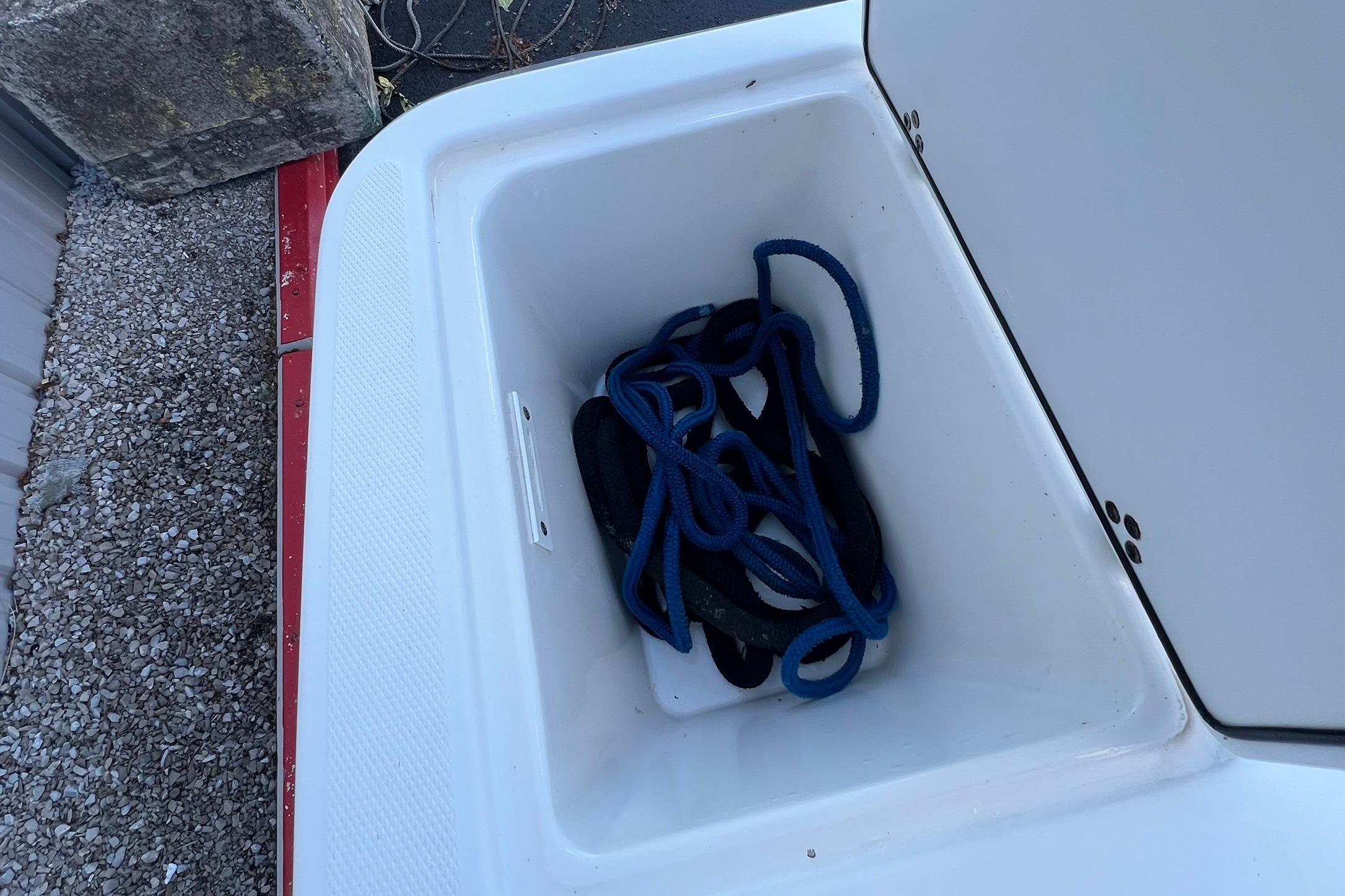 Storage compartment on a 2006 Edgewater 245CC boat with coiled blue rope inside.