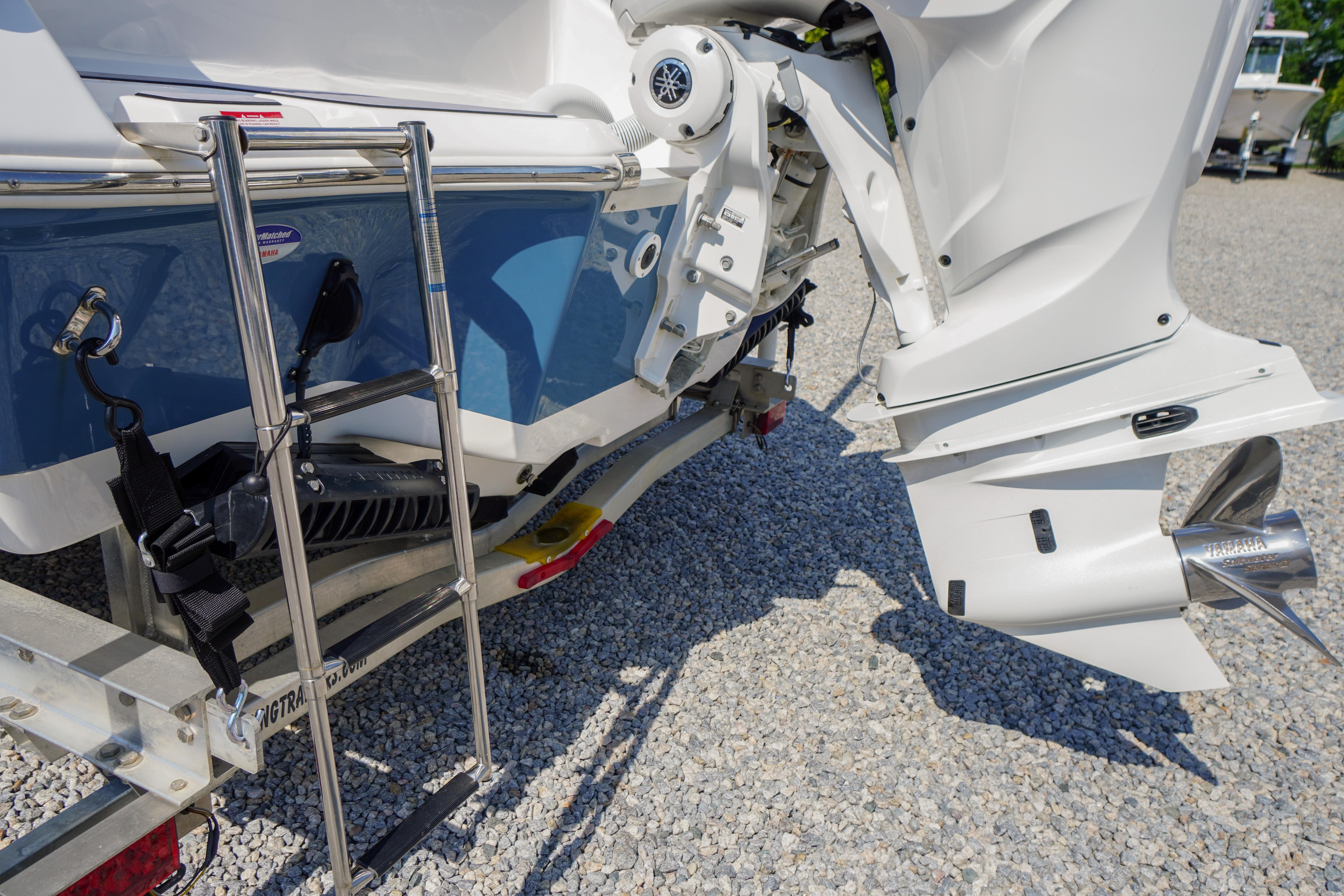 2025 Tidewater 232 SS boat stern with ladder and outboard motor on gravel.