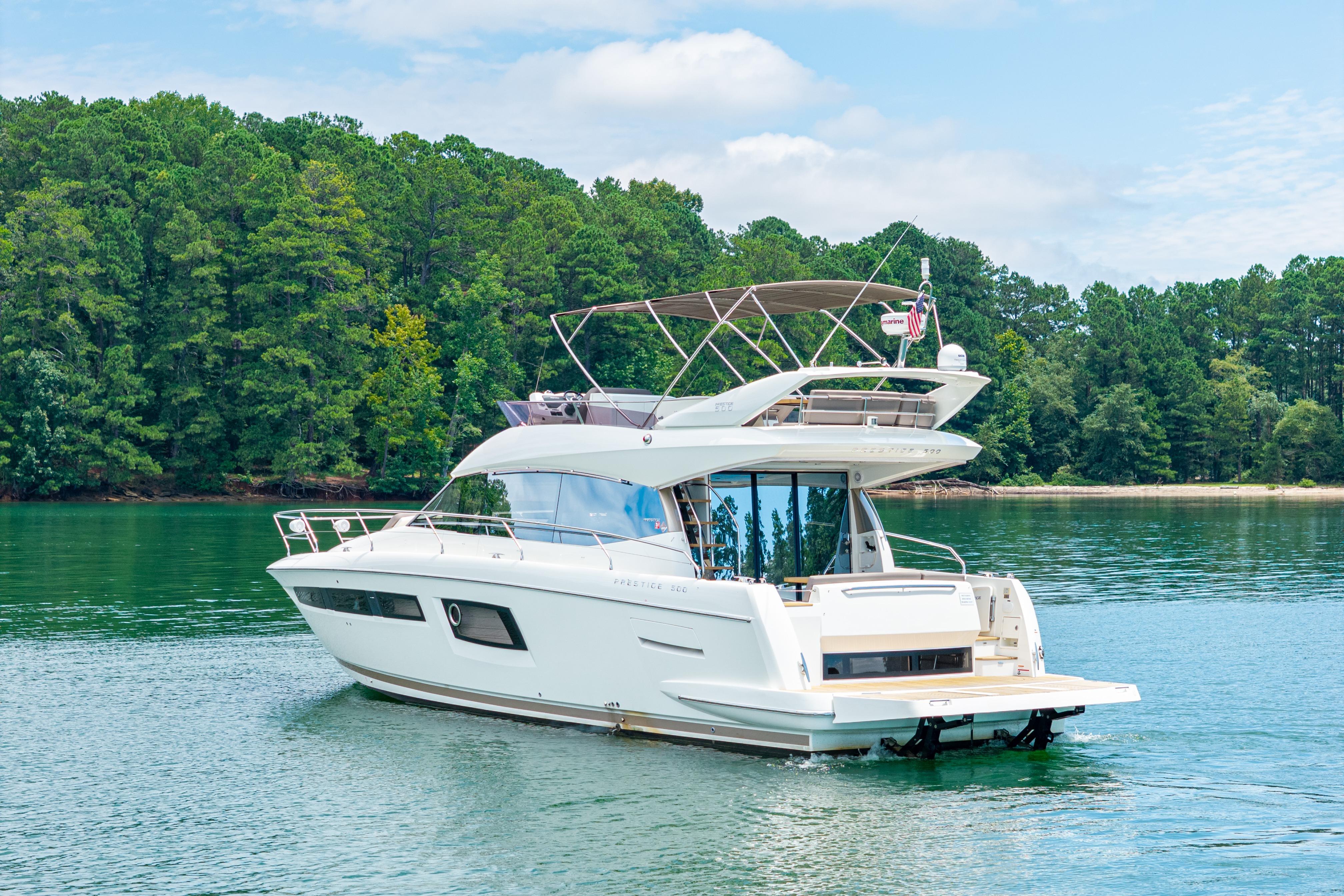 Luxury 2017 Prestige 500 yacht cruising on a serene lake with lush green forest backdrop.
