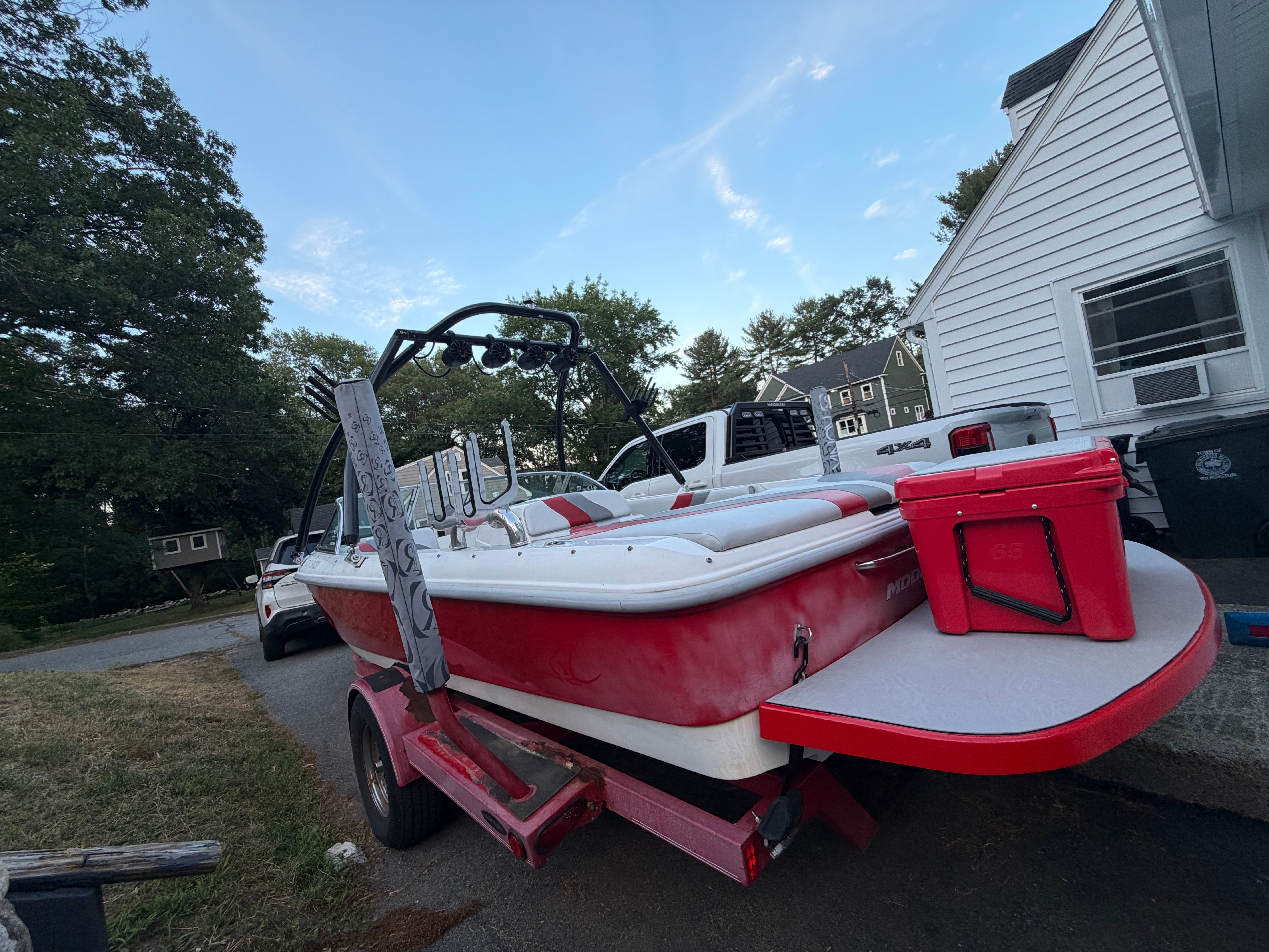 A red Moomba Outback boat is on a trailer next to a house.