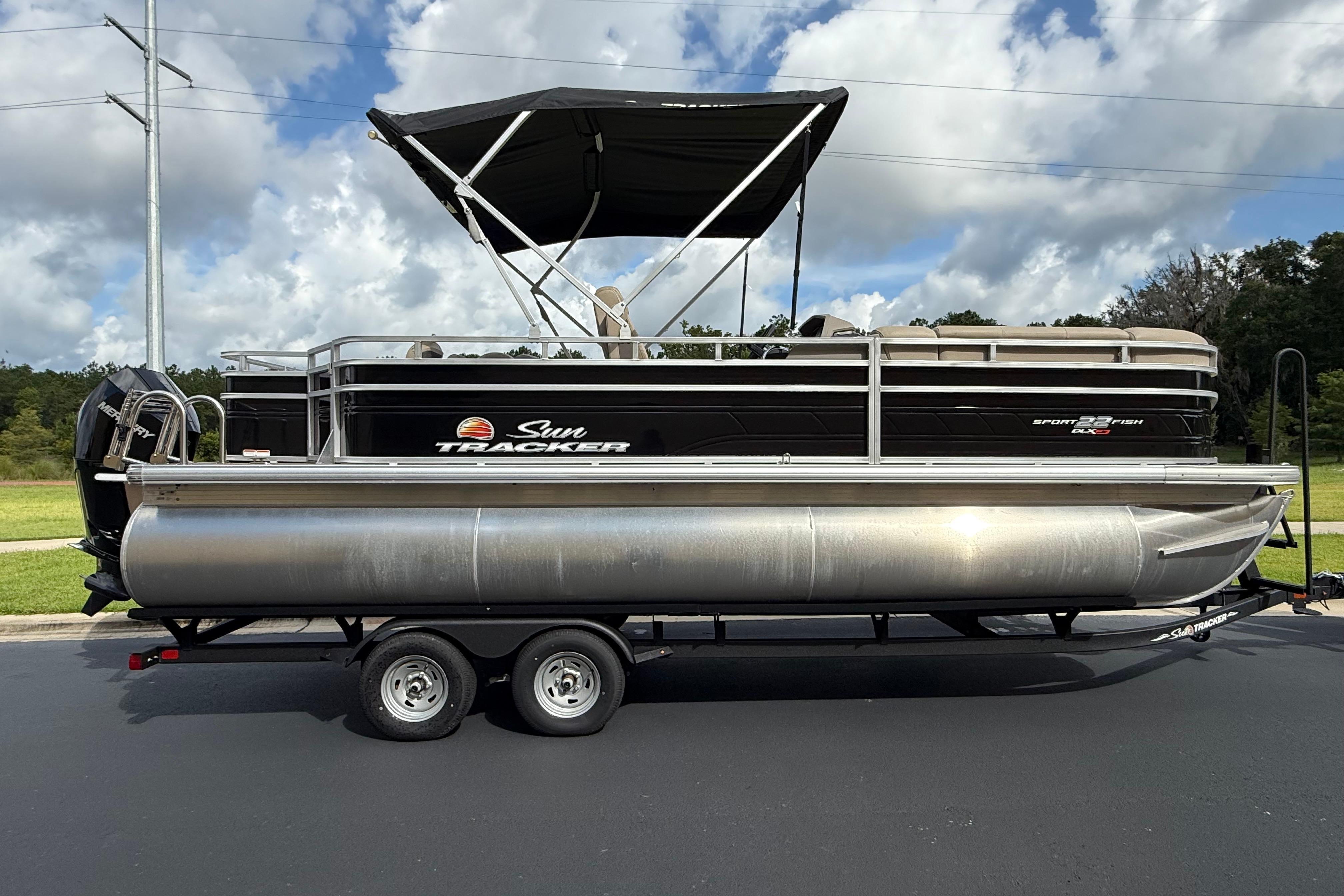 2024 Sun Tracker SportFish 22 XP3 pontoon boat on trailer, under a cloudy sky.