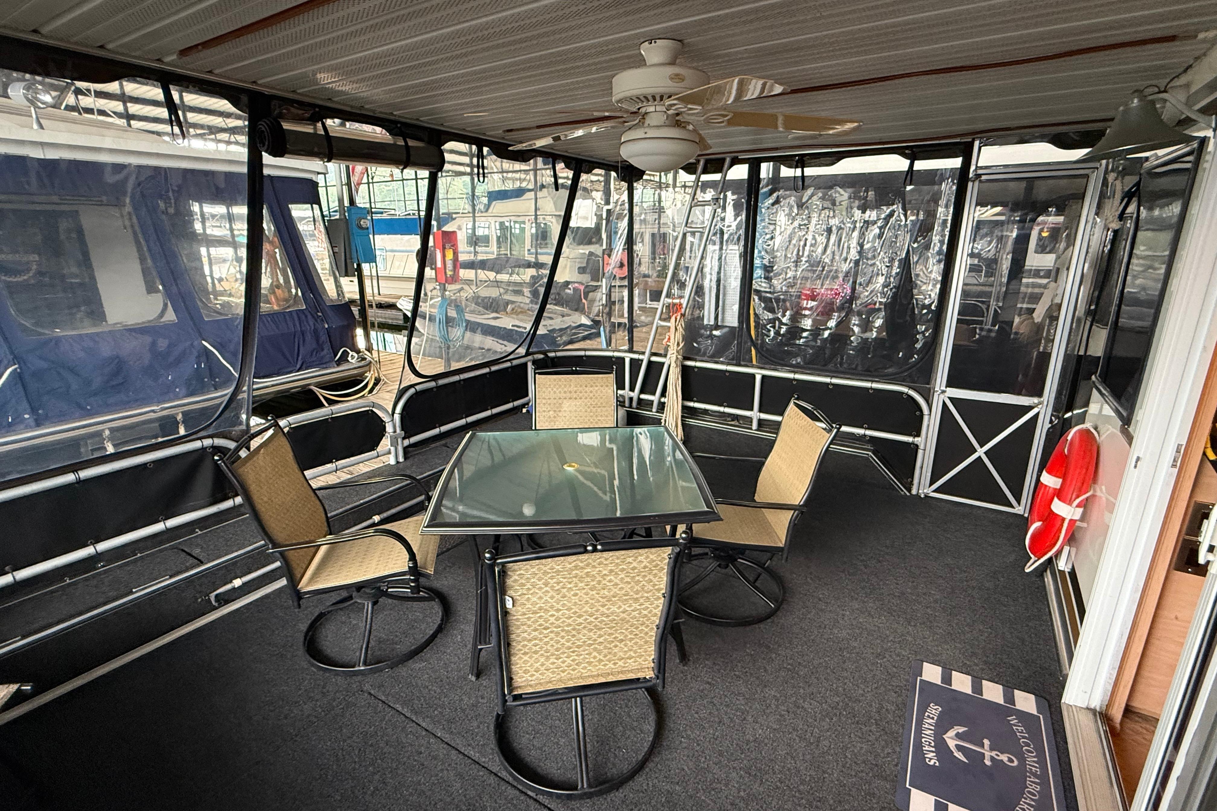 Outdoor seating area on a 1998 Sumerset 16x76 houseboat with glass table and chairs.