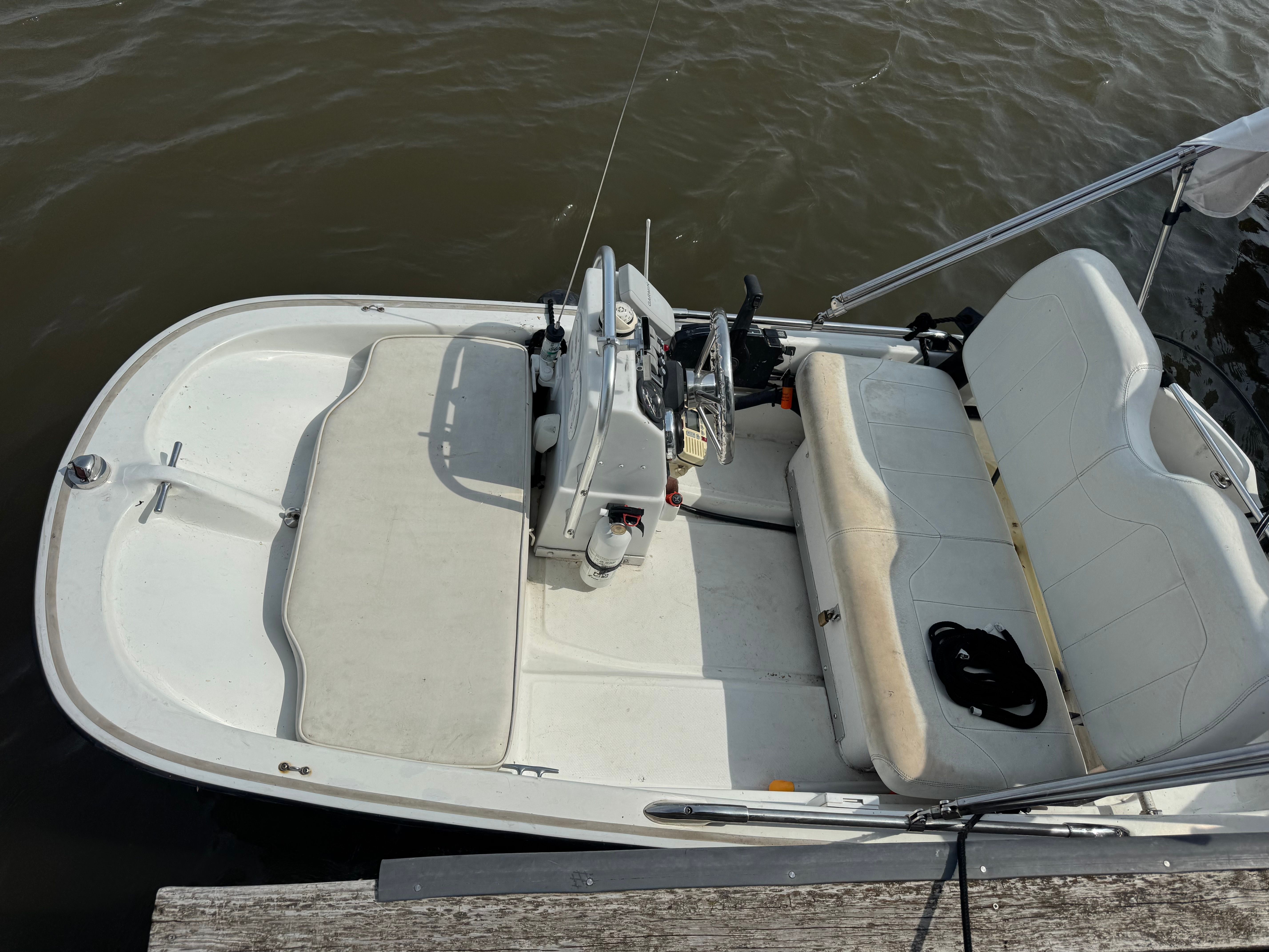 A white boat with bench seating and a helm console, docked at a pier.