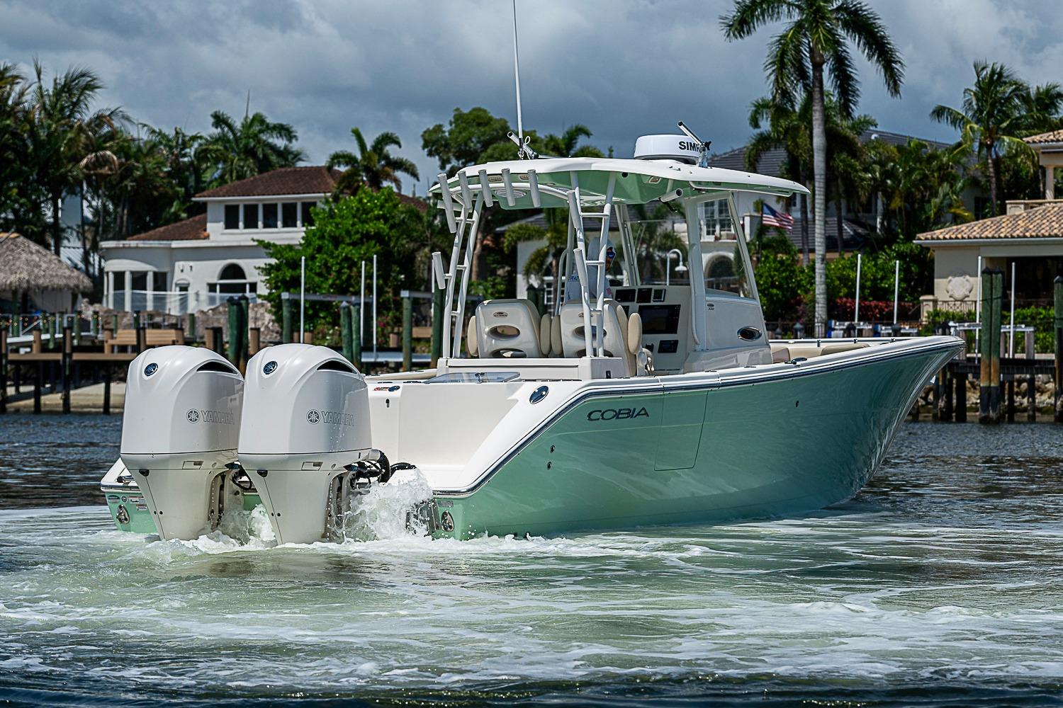 2019 Cobia 320 Center Console boat cruising near waterfront homes with palm trees.