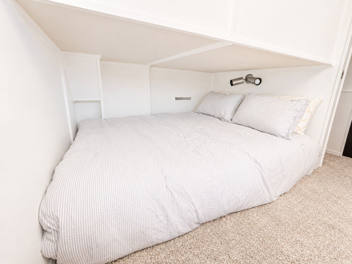 A cozy bed in a houseboat with white bedding and carpeted floor.