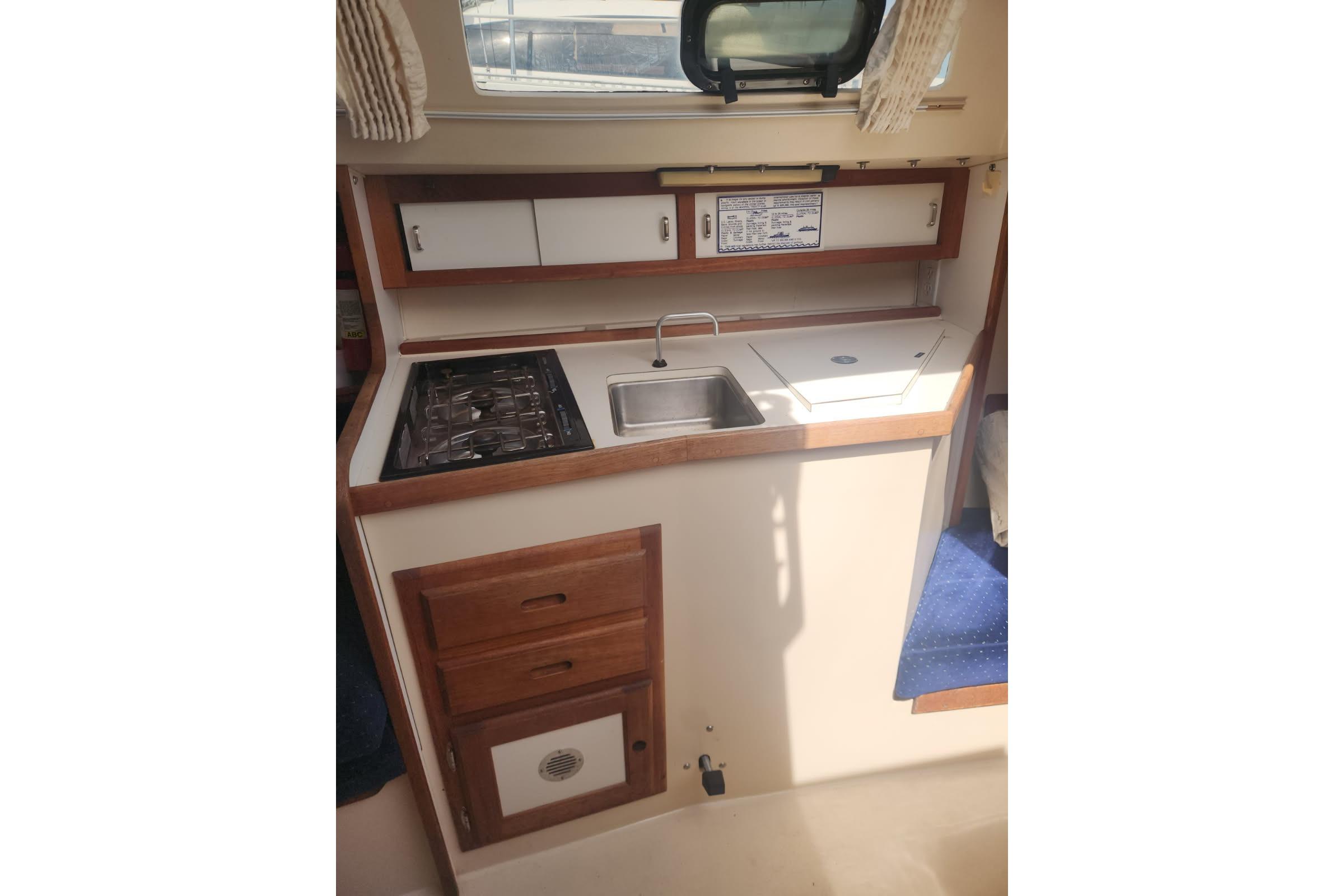 1990 Catalina Capri boat kitchen with stove, sink, and storage cabinets.