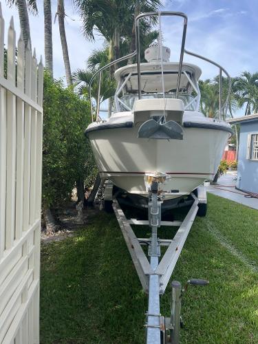 2011 Boston Whaler 235 Conquest boat on trailer, parked on grass near palm trees.