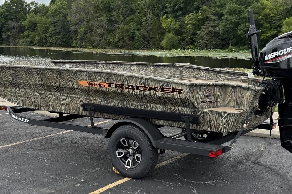 2026 Tracker Grizzly 1756 T Marsh boat with camouflage design on a trailer by a lake.
