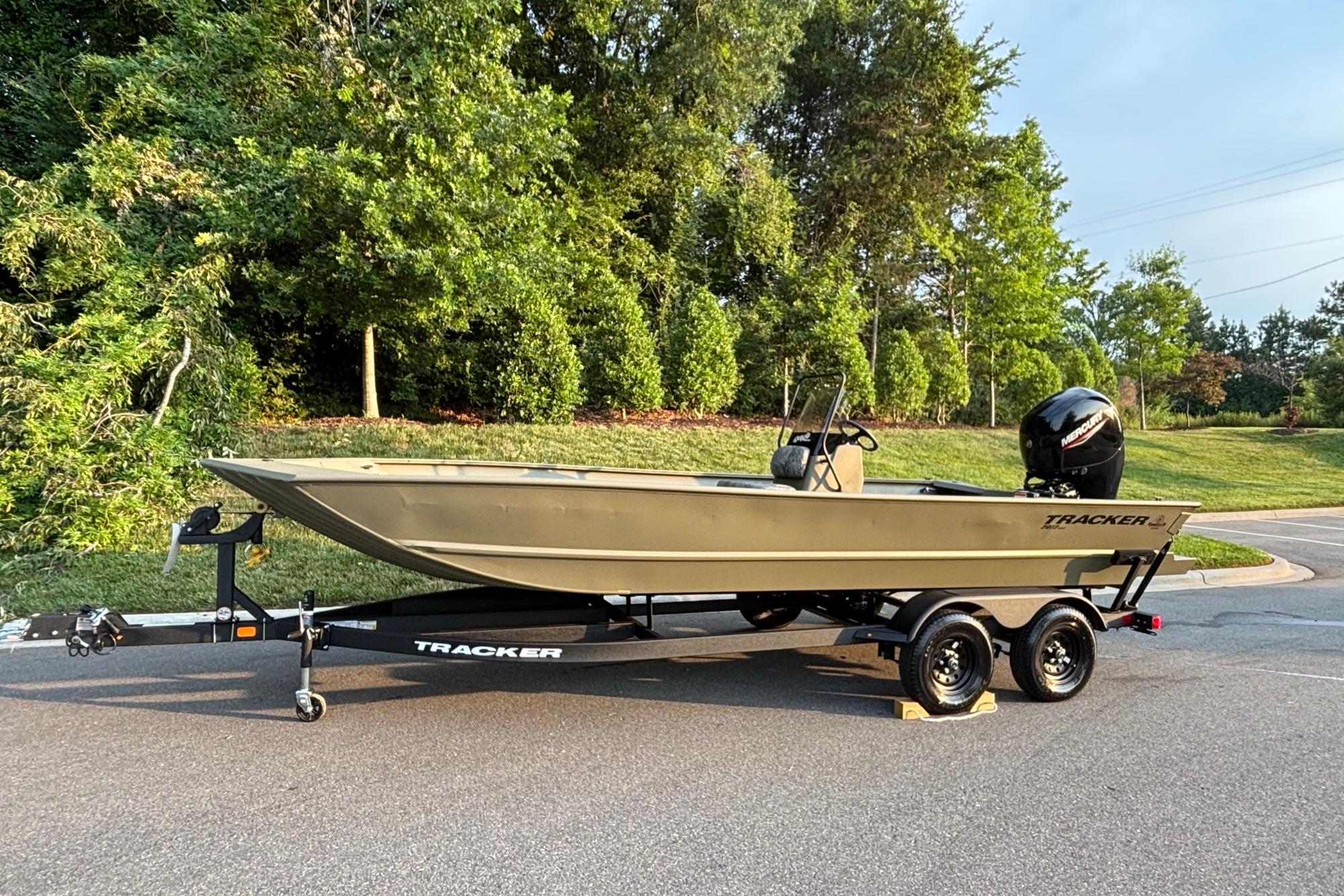 2026 Tracker Grizzly 2072 CC boat on trailer, parked outdoors near lush greenery.