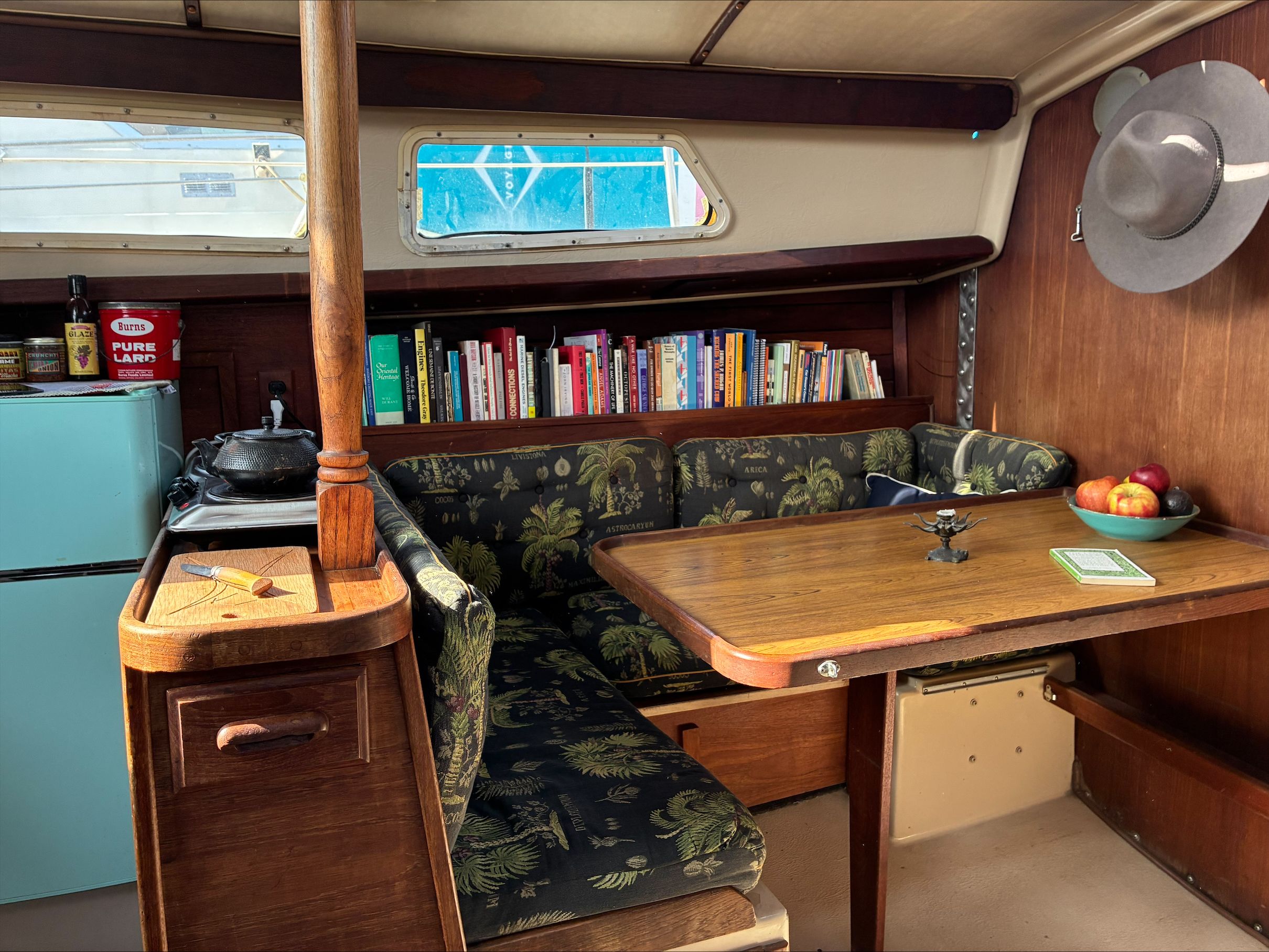 Interior of a 1980 Newport 30 with a cozy seating area, books, and a small kitchen.