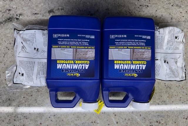 Two blue bottles of aluminum cleaner and restorer on a concrete surface.