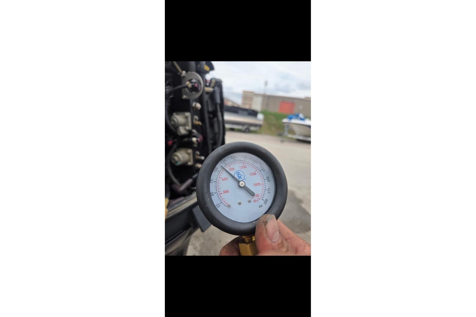 Hand holding pressure gauge near Tracker Pro Team 190 TX boat engine, 2015 model.