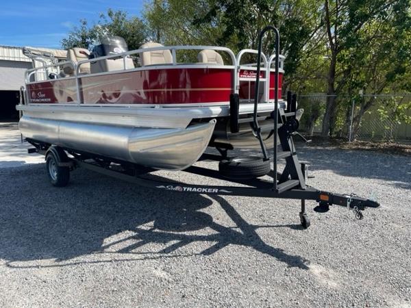 2024 Sun Tracker Bass Buggy 18 DLX pontoon boat on a trailer in a gravel lot.