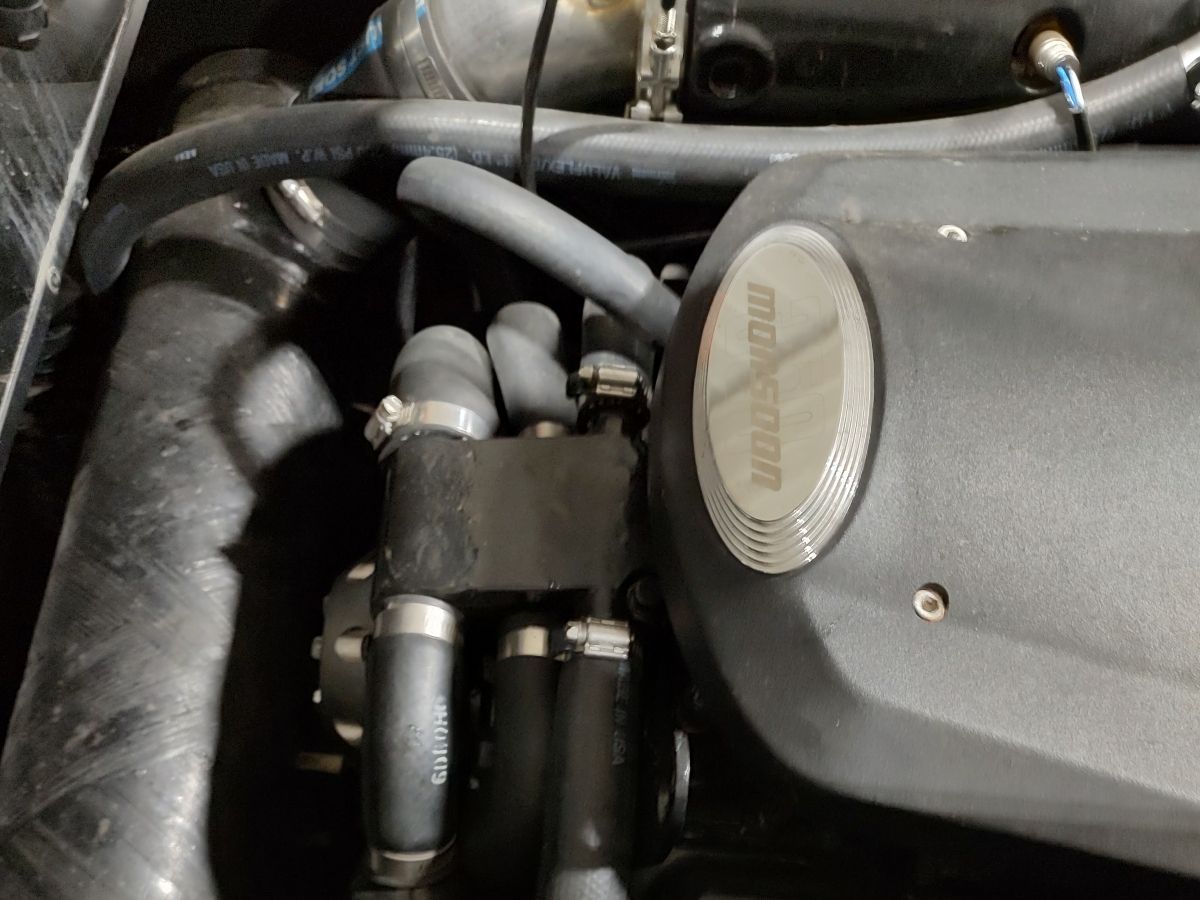 Close-up of an engine compartment with hoses and an engine cover featuring "Monsoon" logo.