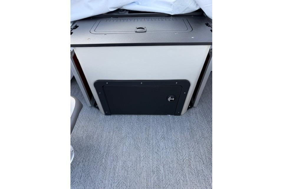 2026 Sun Tracker Fishin' Barge 22 XP3 storage compartment with secure latch on carpeted floor.