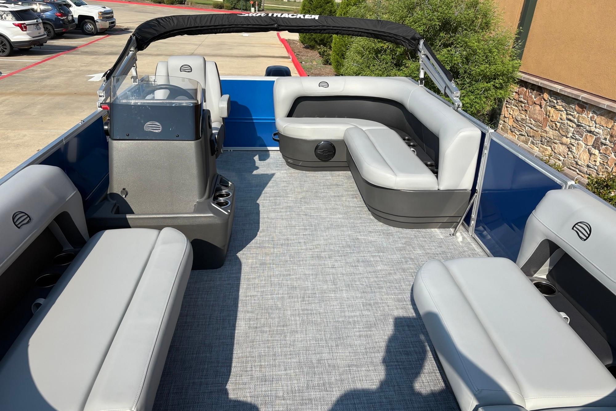 2026 Sun Tracker Party Barge 16 DLX interior with gray seating and helm, parked outdoors.
