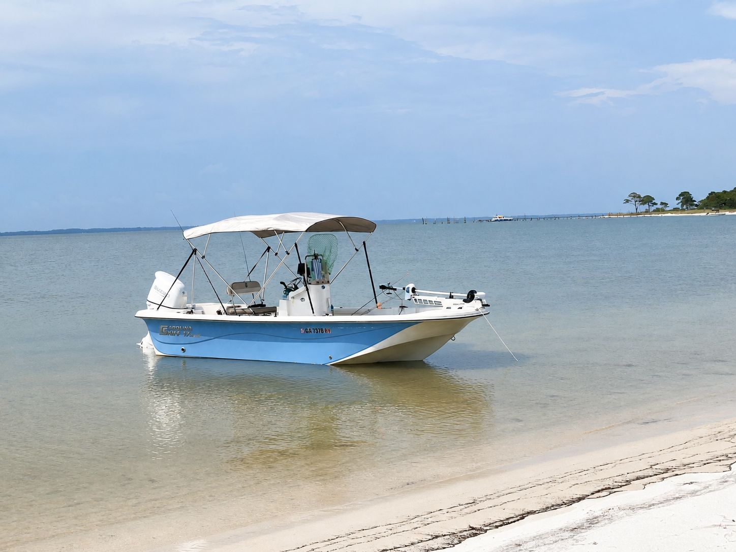 A 2022 Carolina Skiff 17 LS boat is in shallow water near a sandy beach.