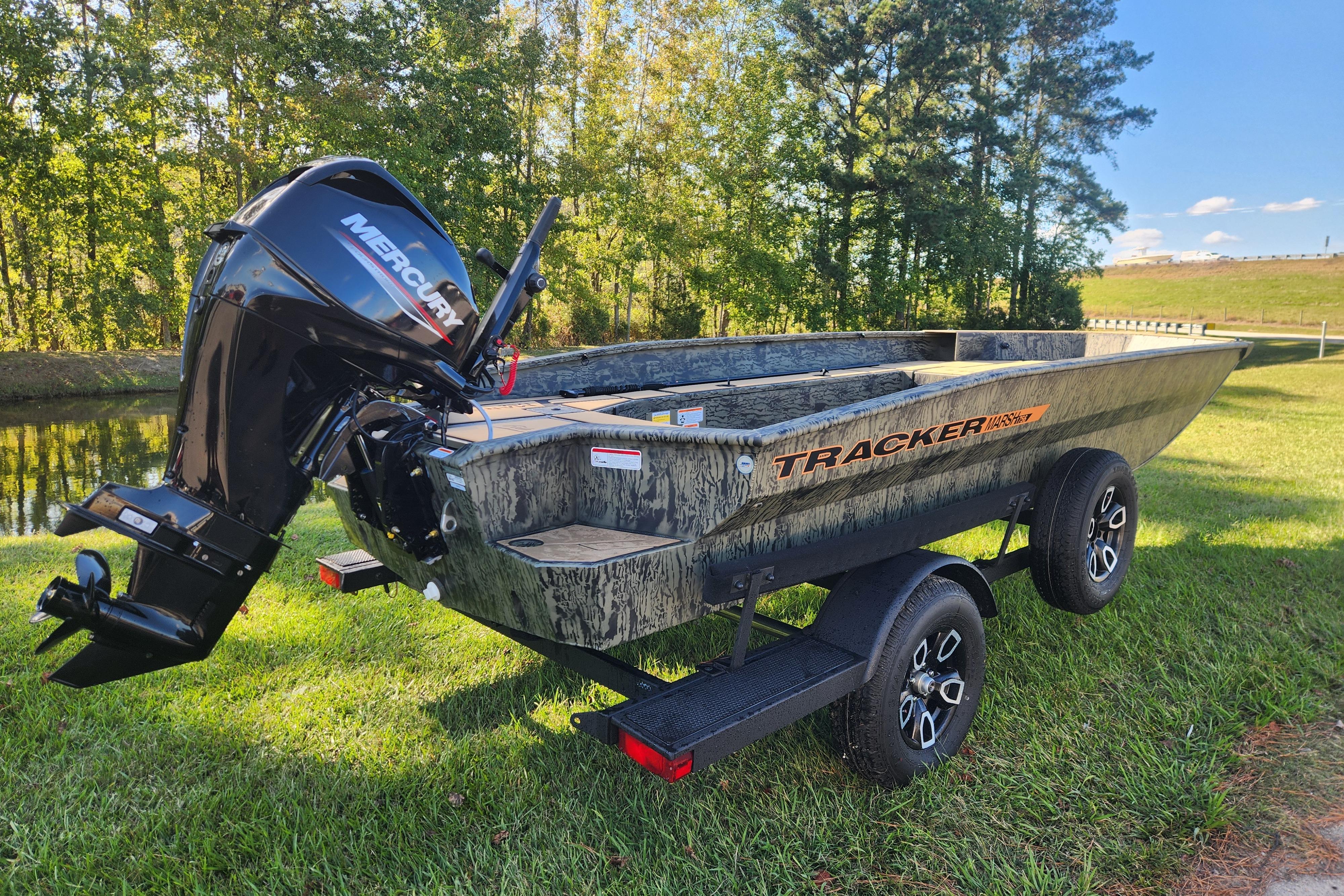 2026 Tracker Grizzly 1756 T Marsh boat on trailer, parked on grass by a pond.