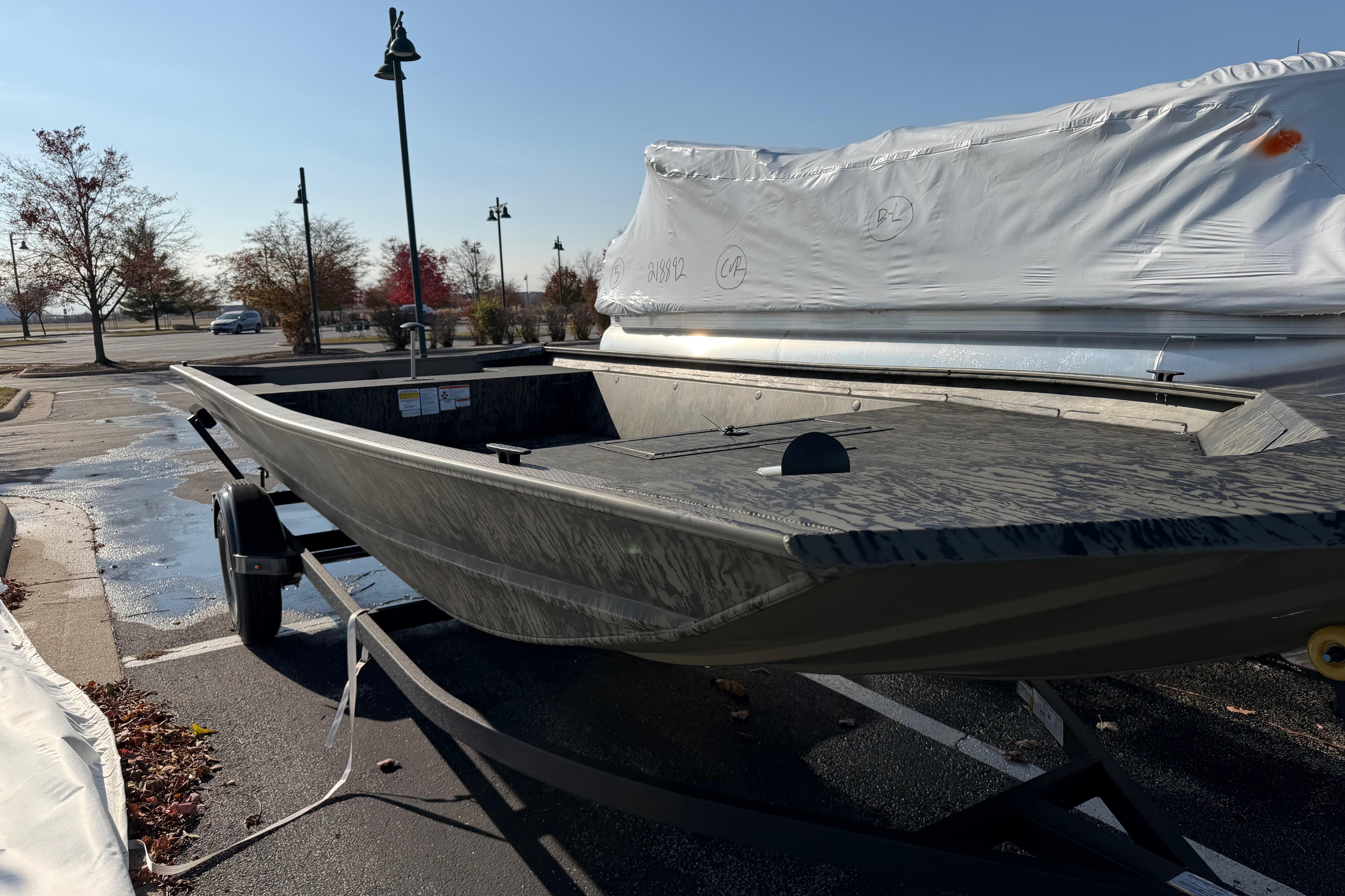 2026 Tracker Grizzly 1860 Utility boat on trailer in parking lot, wrapped boats nearby.
