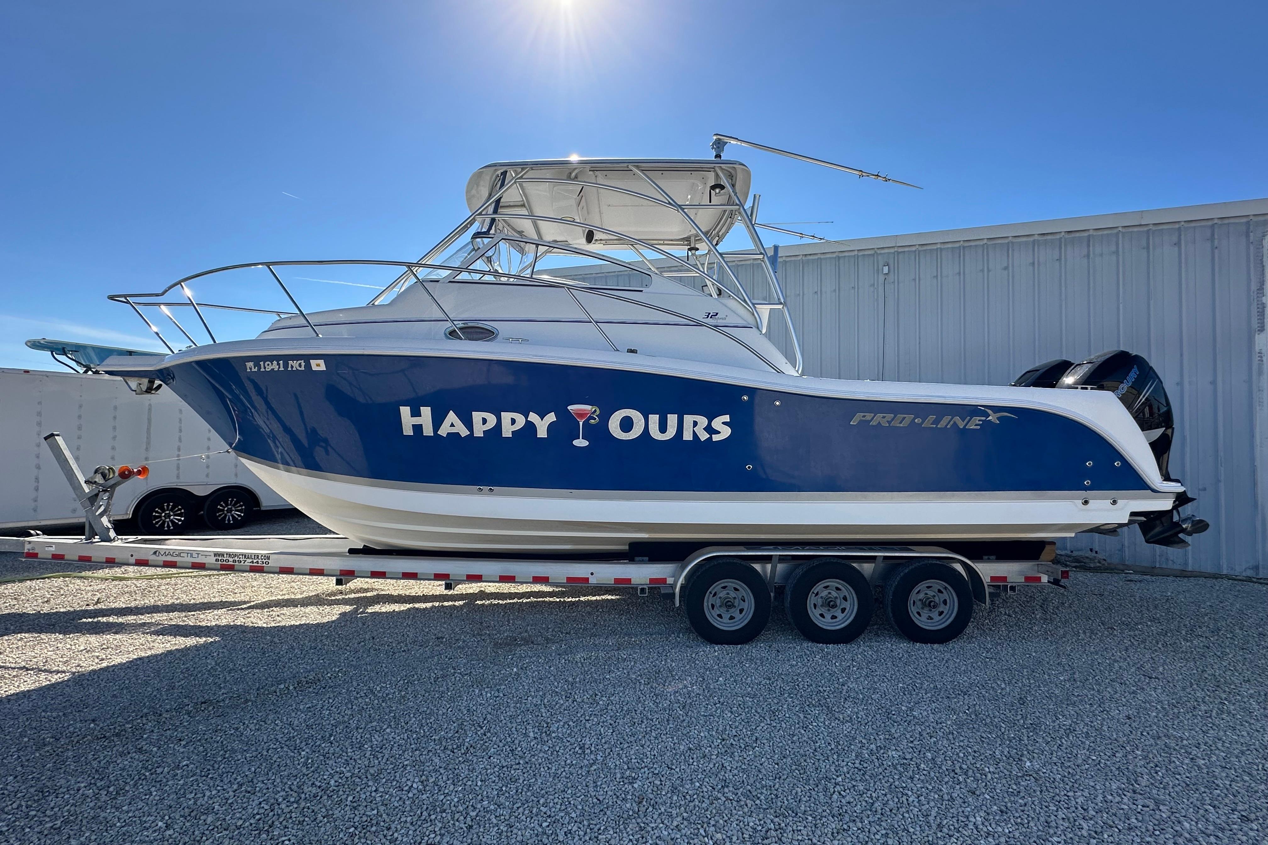 2006 Pro-Line 32 Express boat named "Happy Ours" on a trailer, parked outdoors.