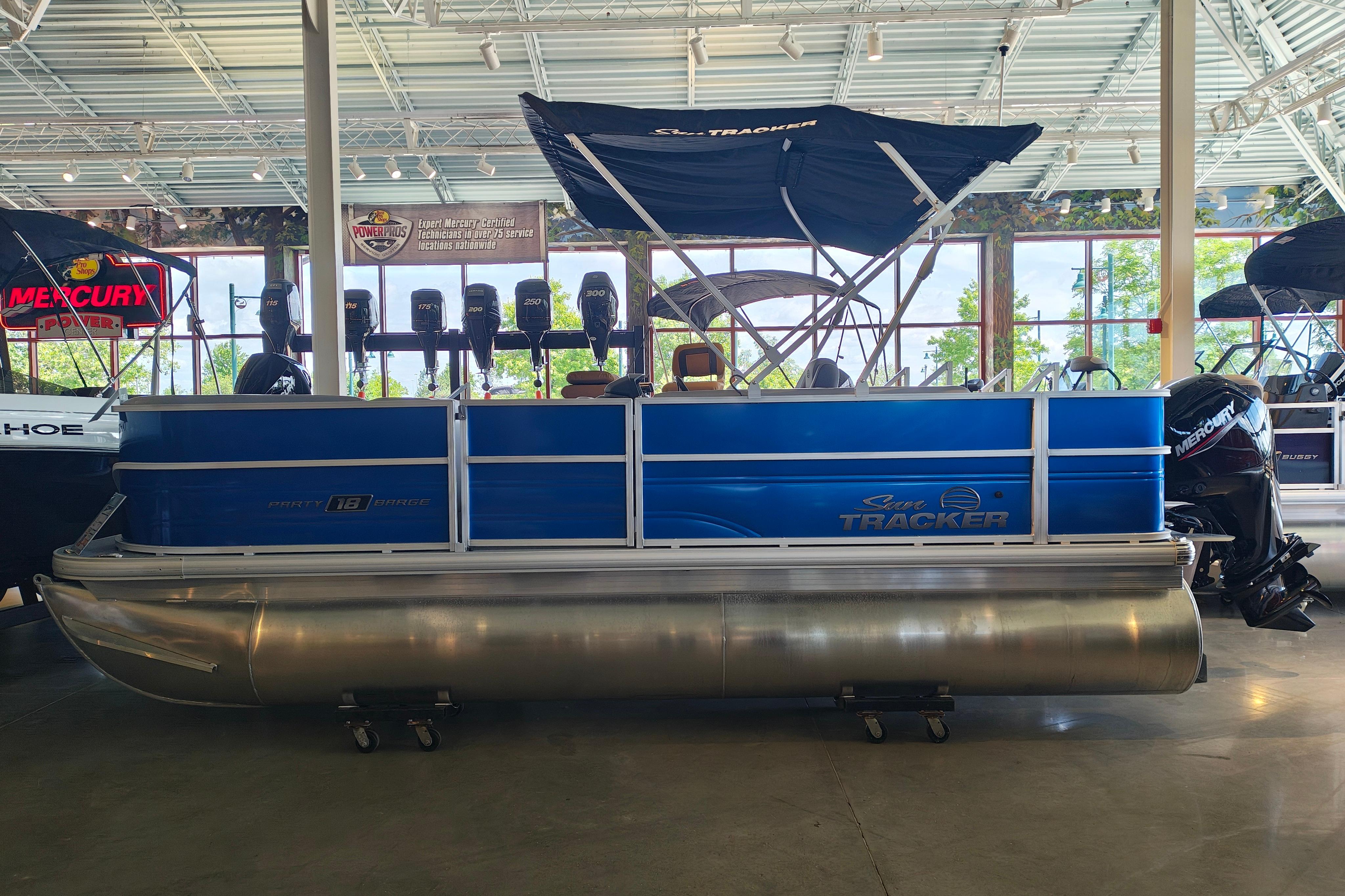 A blue pontoon boat with a canopy is displayed in a showroom.