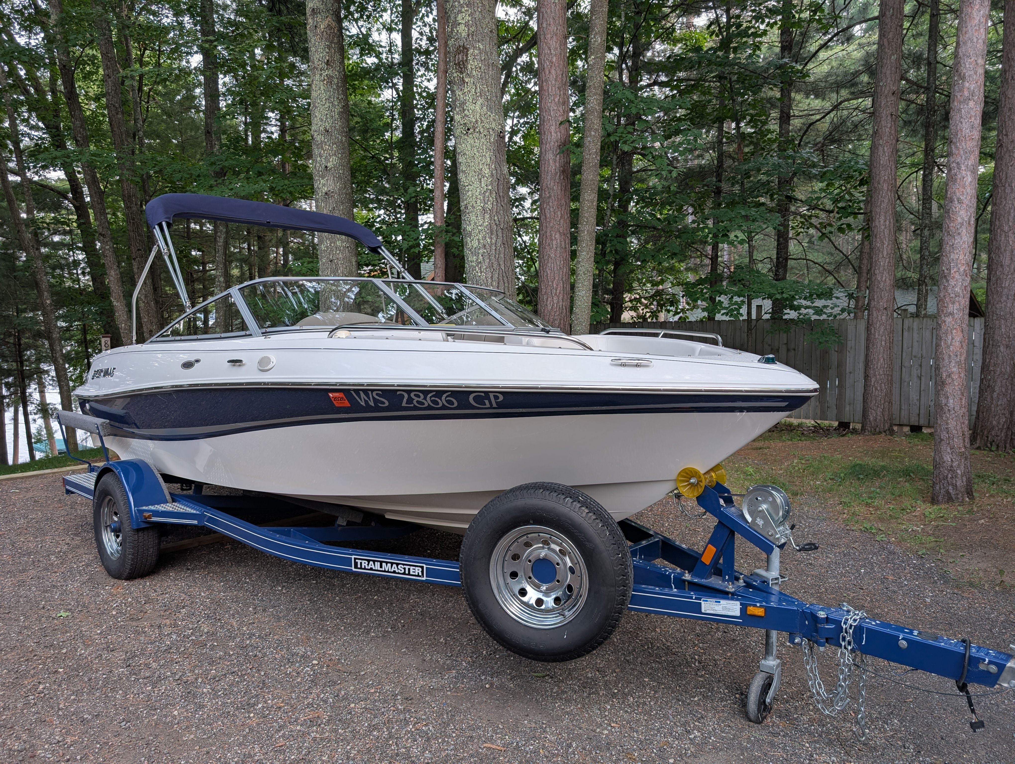 A 2004 Four Winns 190 Horizon on a blue trailer parked in a wooded area.