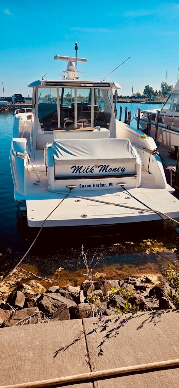 A 2017 Tiara Yachts Q44 docked in the harbor. The name "Milk Money" is visible.