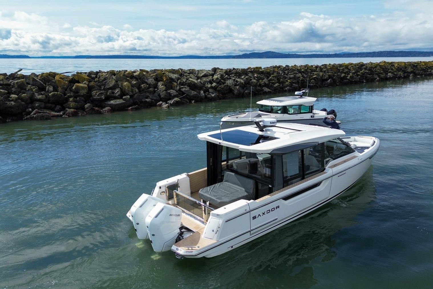 2026 Saxdor 400 GTC boat cruising near rocky shoreline under cloudy sky.
