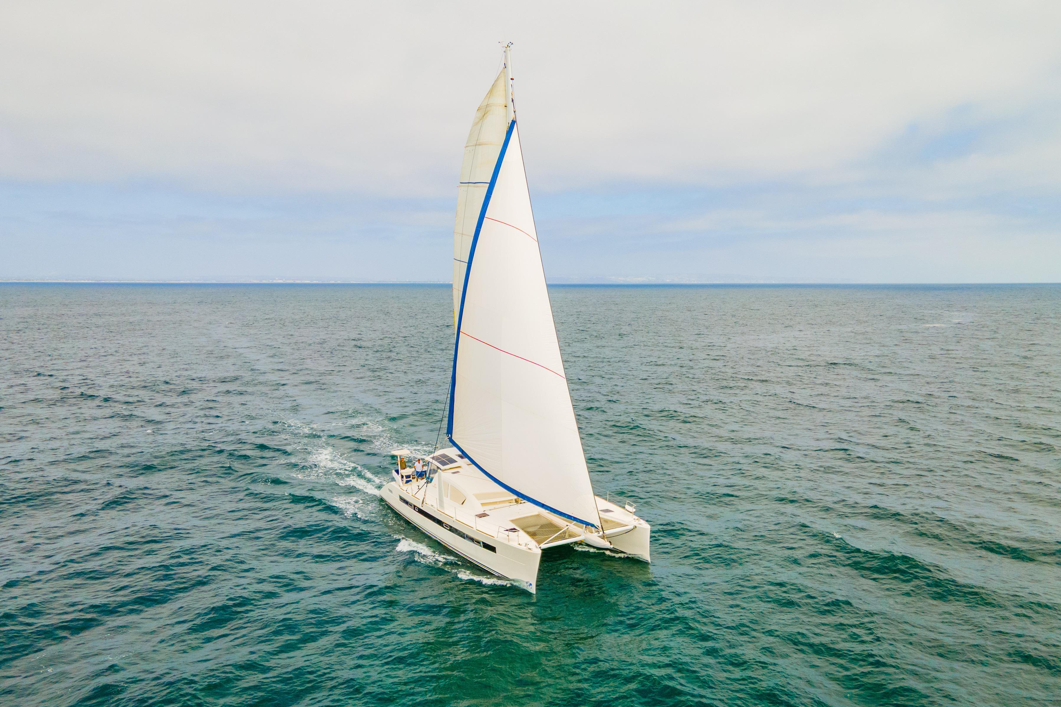 Catana 65 catamaran sailing on open sea, 2009 model, with white sails and blue trim.