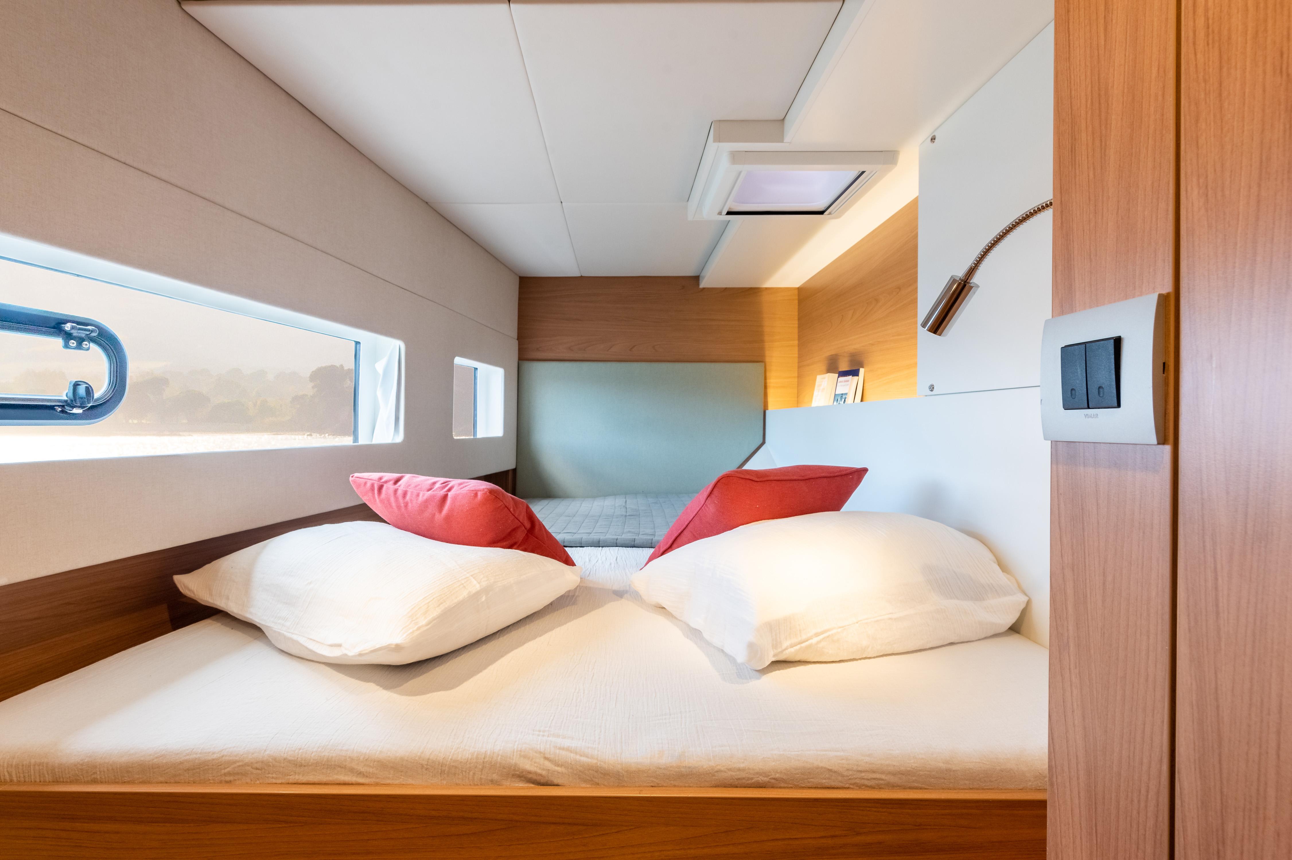 Modern yacht cabin interior with cozy bed, red pillows, and sleek wooden design, Bali CATSMART 2025.