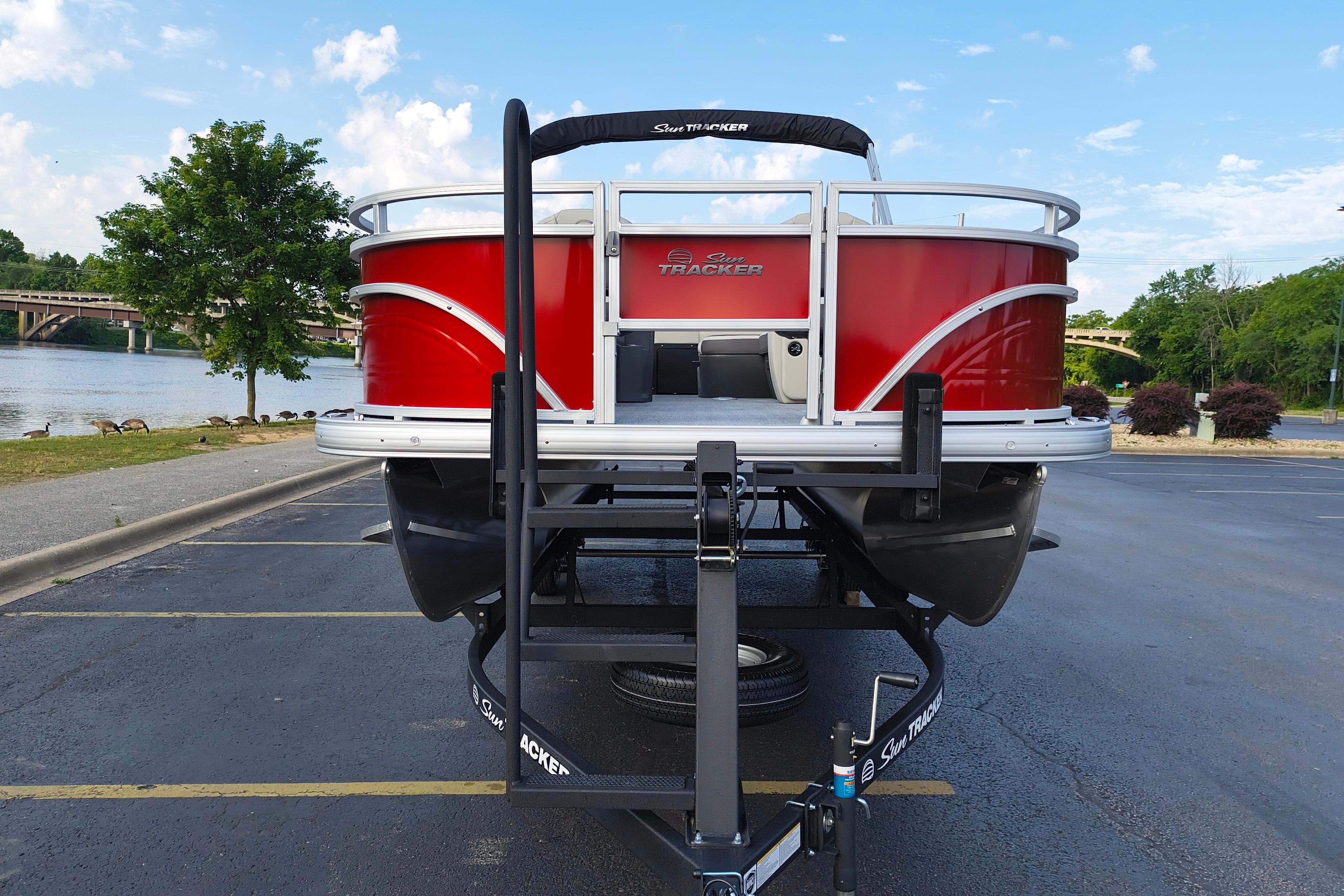 2026 Sun Tracker Fishin' Barge 22 DLX pontoon boat on trailer by a scenic river.