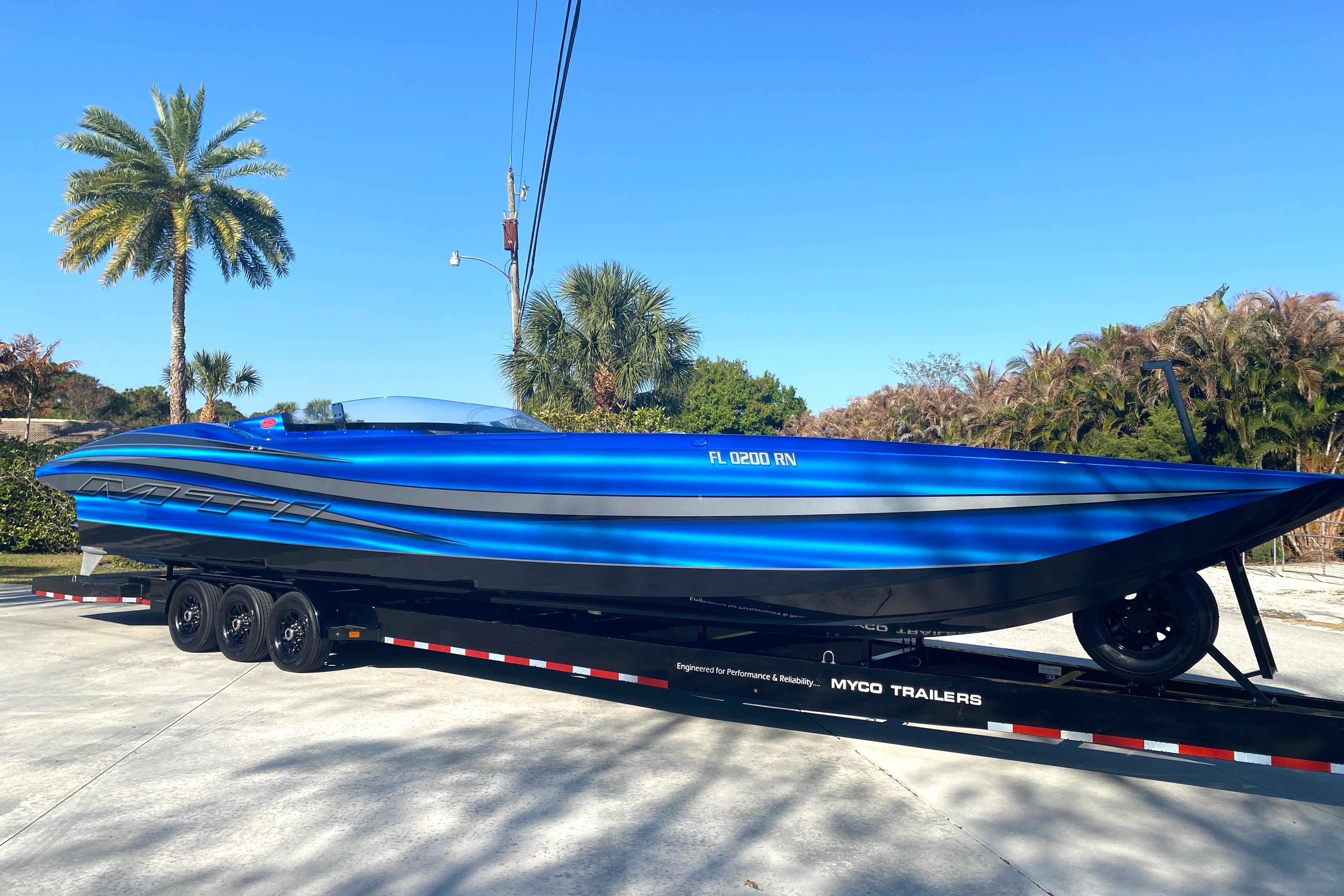 Blue 2016 MTI 44 RP speedboat on trailer, parked outdoors under clear sky.