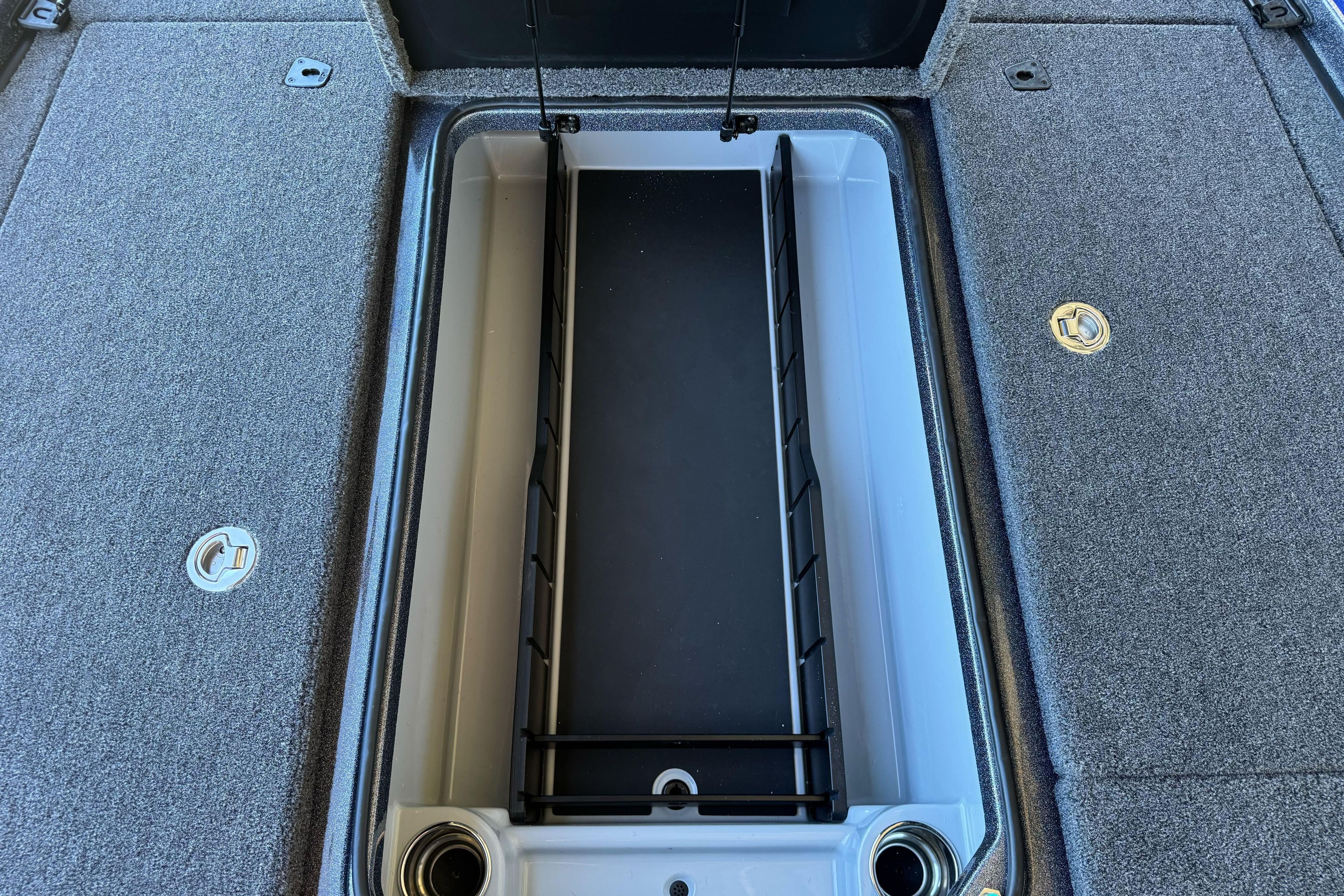 Open storage compartment in 2026 Triton 21XP Patriot boat, featuring carpeted surfaces and metal latches.