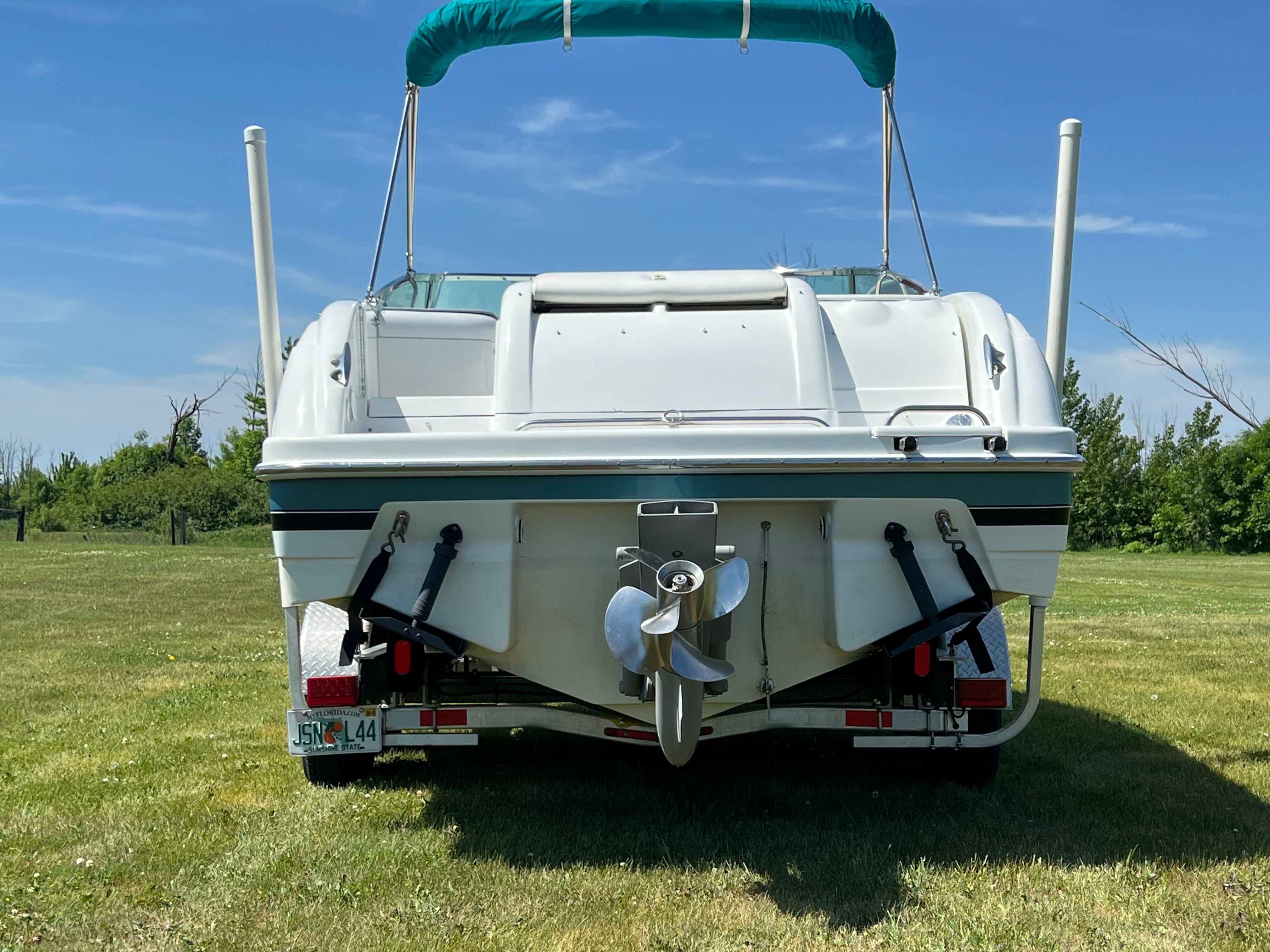 A white boat with a green sunshade is on a trailer in a grassy area.
