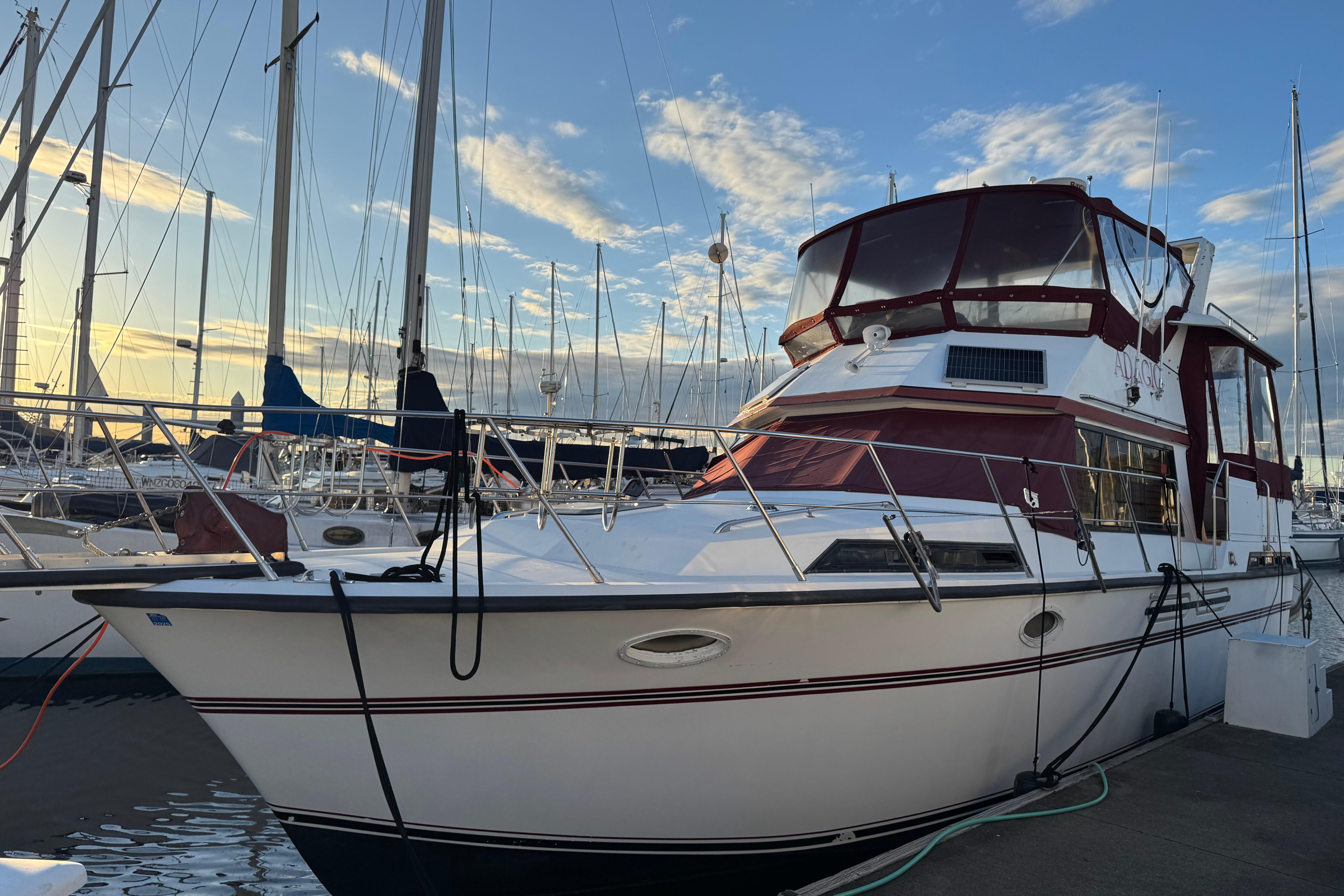 1987 President 37 yacht docked at marina, featuring maroon accents and clear sky backdrop.